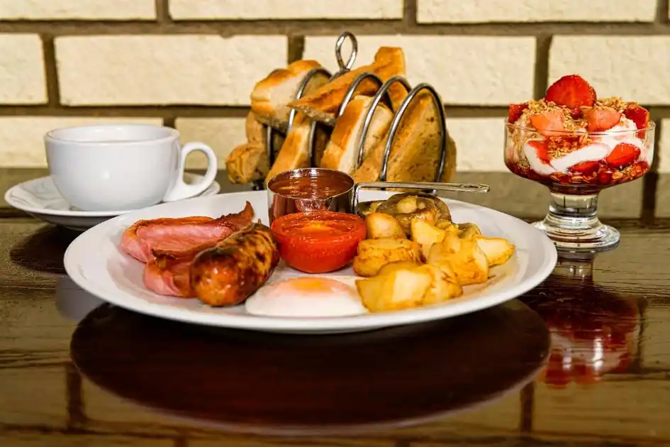 Full English breakfast at Sandcliff Guest House in Cromer, Norfolk, featuring bacon, sausage, fried egg, tomato, mushrooms, potatoes, toast, a cup of tea and a strawberry yoghurt parfait.
