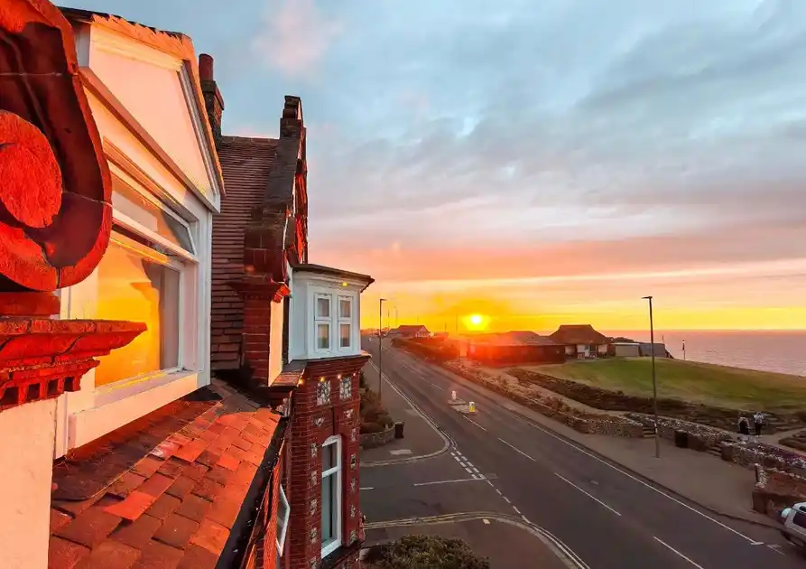 Sunset view from Sandcliff Guest House in Cromer, Norfolk, overlooking the seafront road, clifftop grassland and North Sea, with warm evening sunlight illuminating the Victorian building.