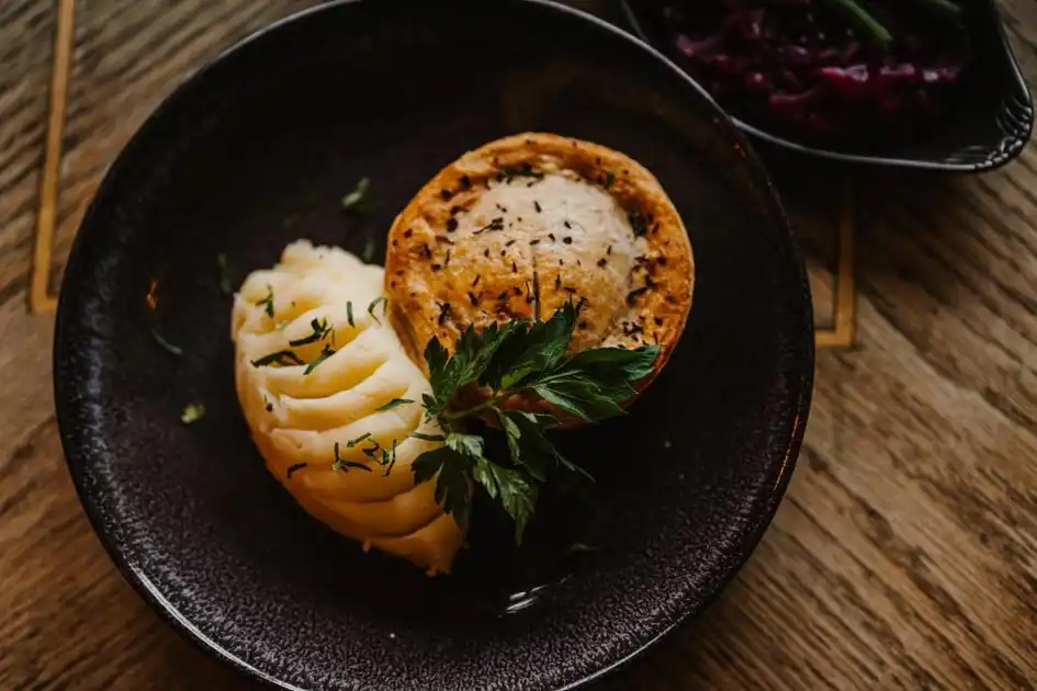Restaurant dish at The Ship Inn in Mundesley, Norfolk, featuring a golden pastry pie served with creamy mashed potatoes, fresh herbs and a side of red cabbage.