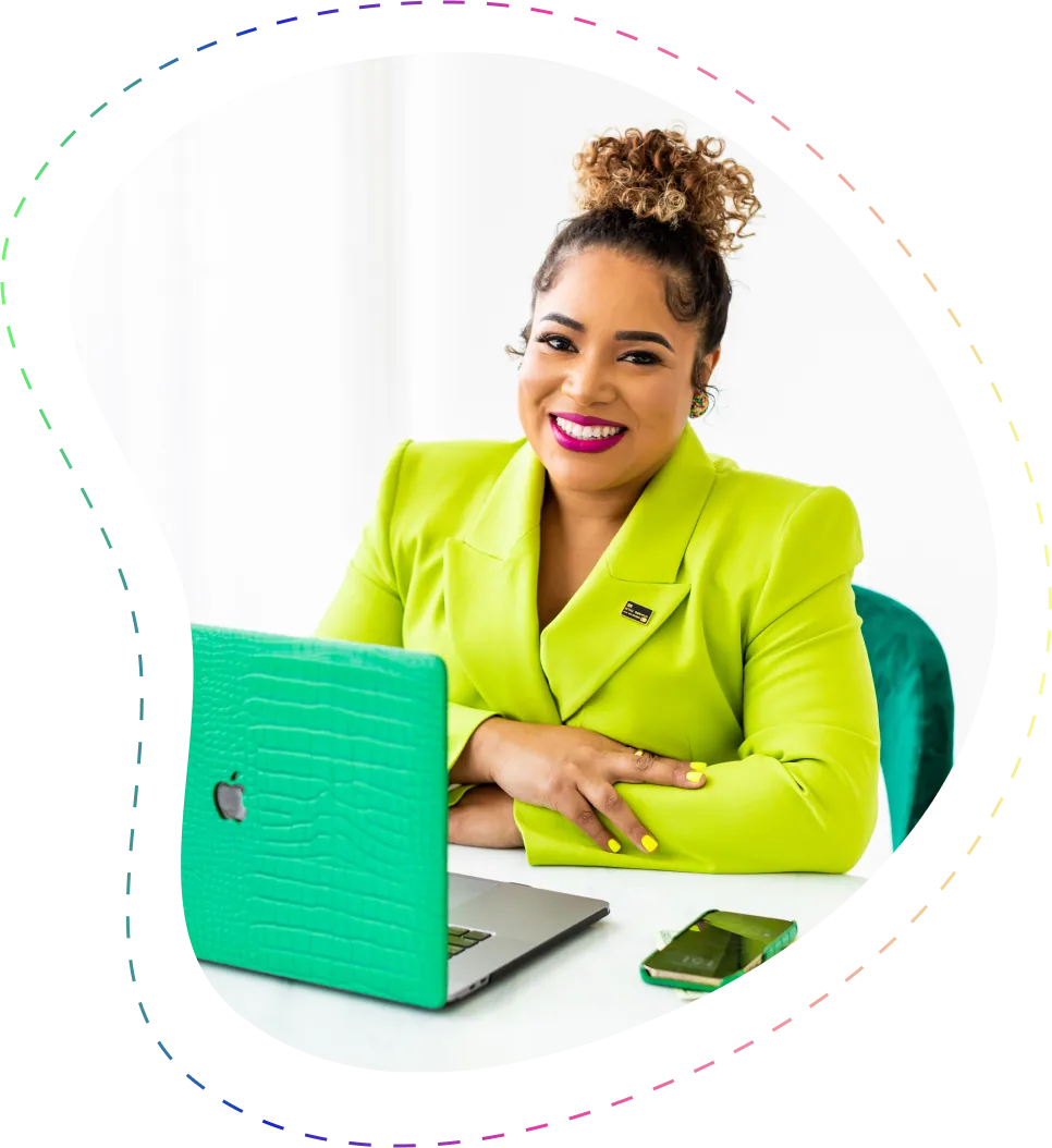 Smiling woman in a bright green blazer sitting at a desk with a green laptop and smartphone.