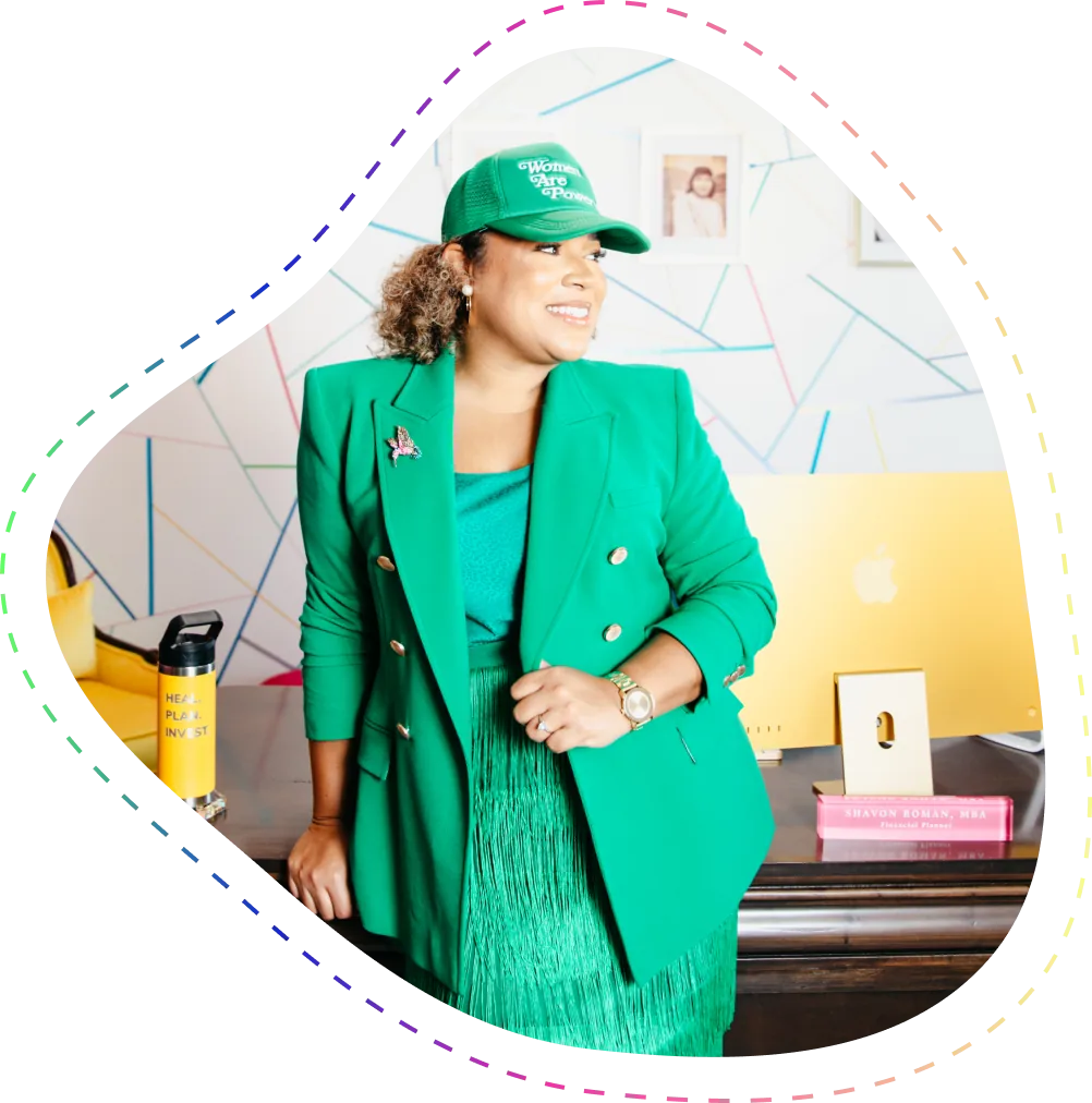Smiling woman in a green blazer and matching hat standing by a desk with a yellow computer and a book labeled 'Shavon Roman, MBA'.