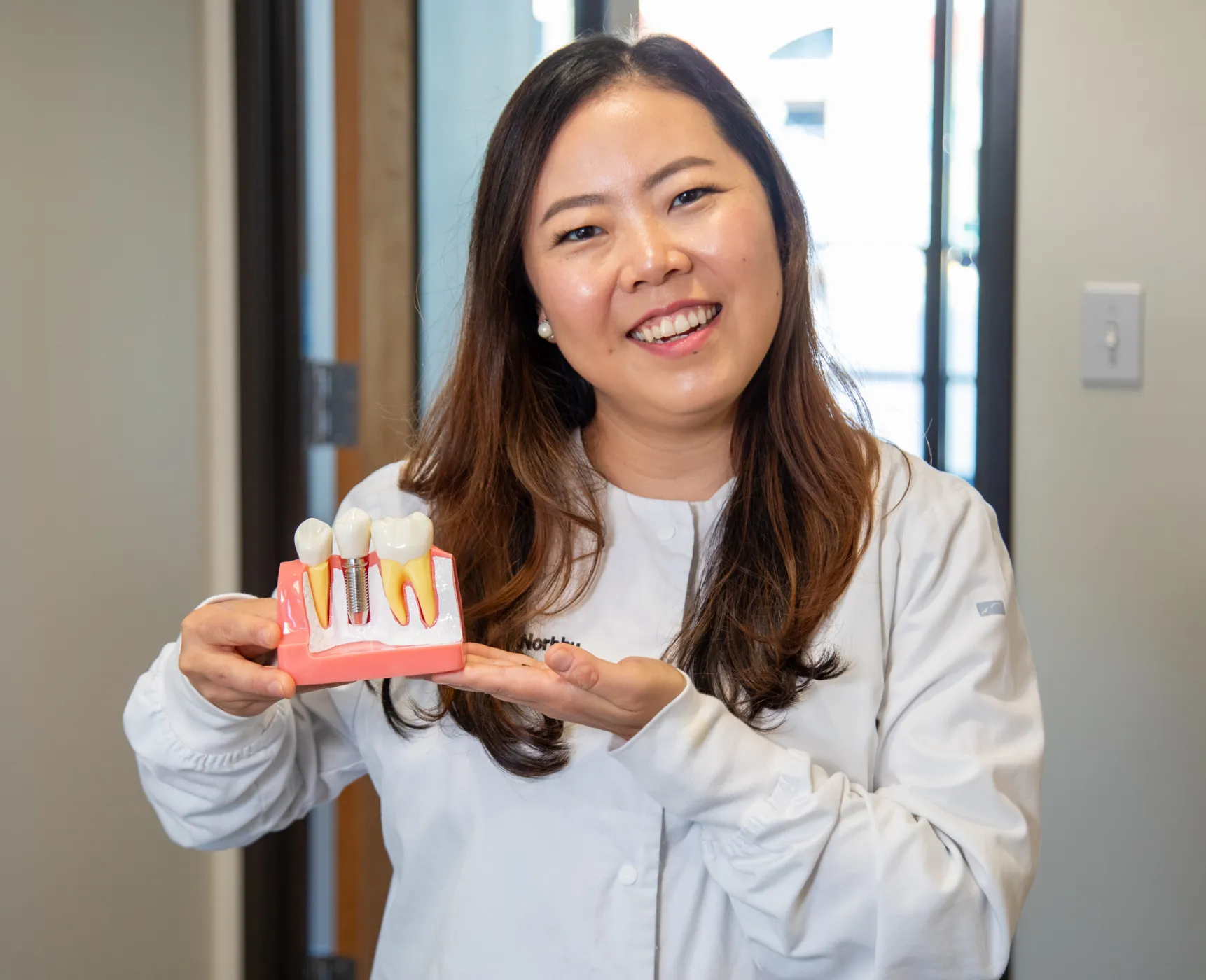 A person in a white coat holding a dental model and smiling.