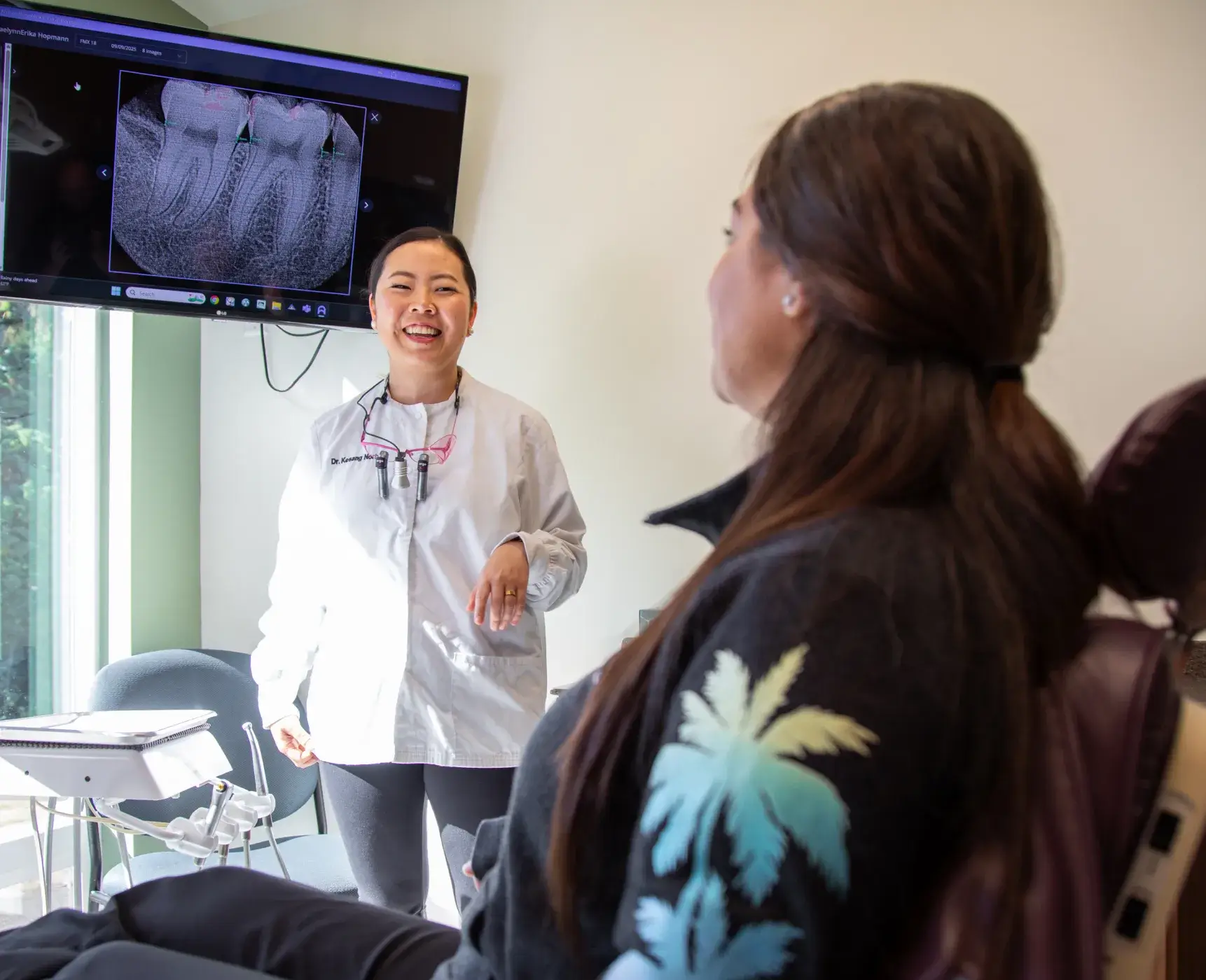 A dentist discusses a dental X-ray with a patient sitting in a chair.