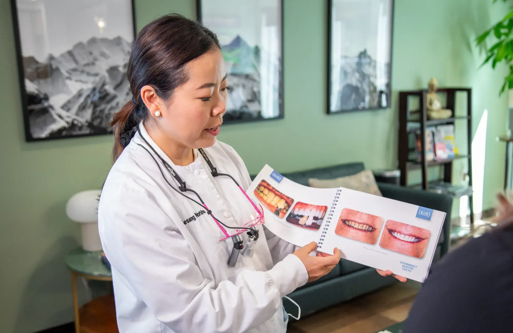A dentist shows a patient a booklet with images of teeth and dental treatments.