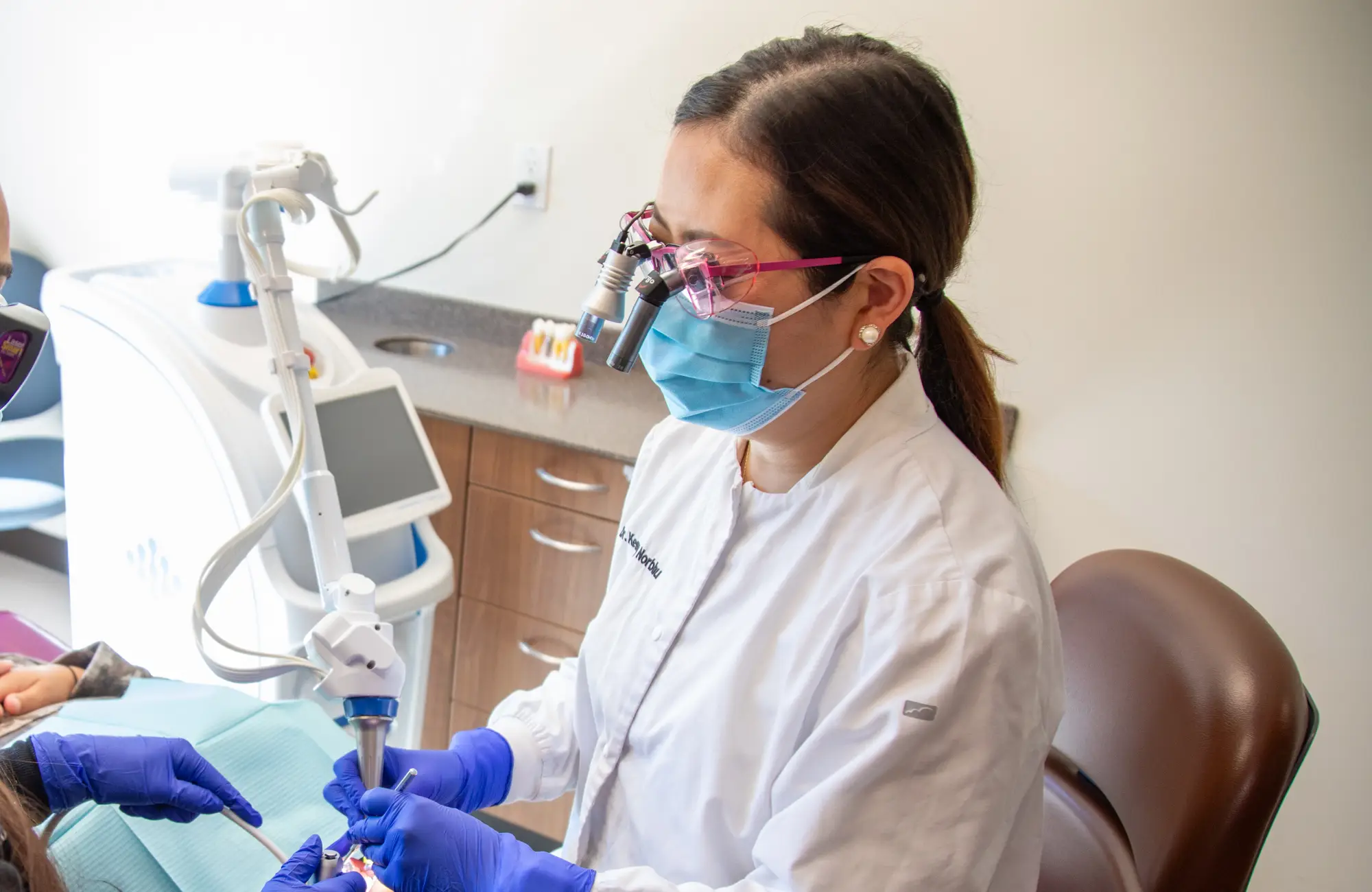 Two dental professionals in masks and gloves perform a procedure on a patient in a dental office.