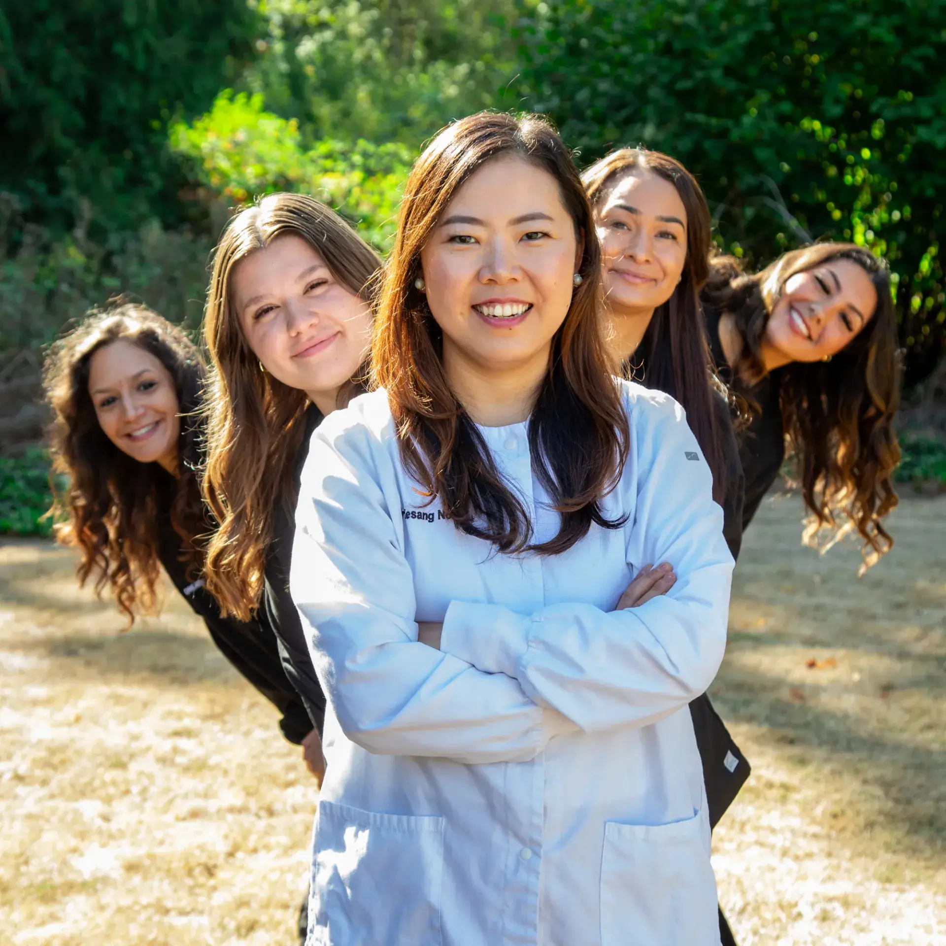 A smiling woman in a white coat stands with four women behind her outside on a sunny day.