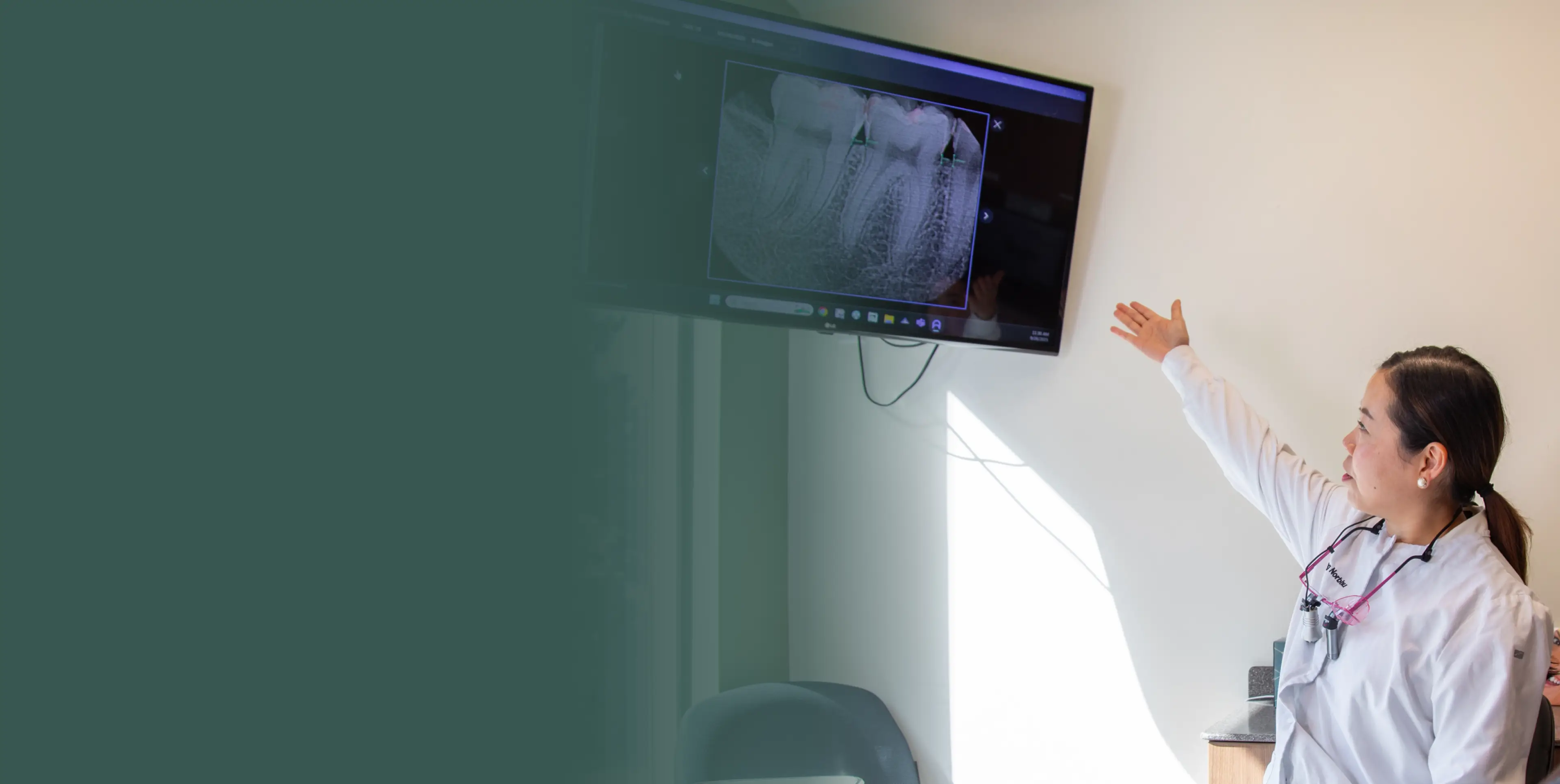 A dentist points at an x-ray on a screen while explaining to a patient.