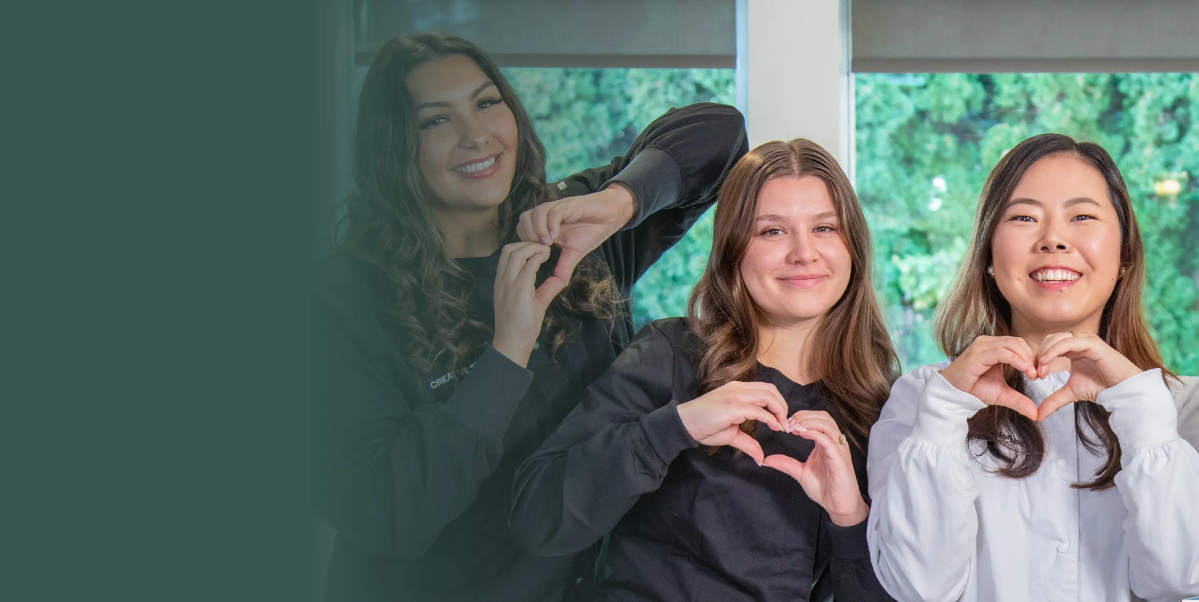 Four people stand indoors, smiling and making heart shapes with their hands.