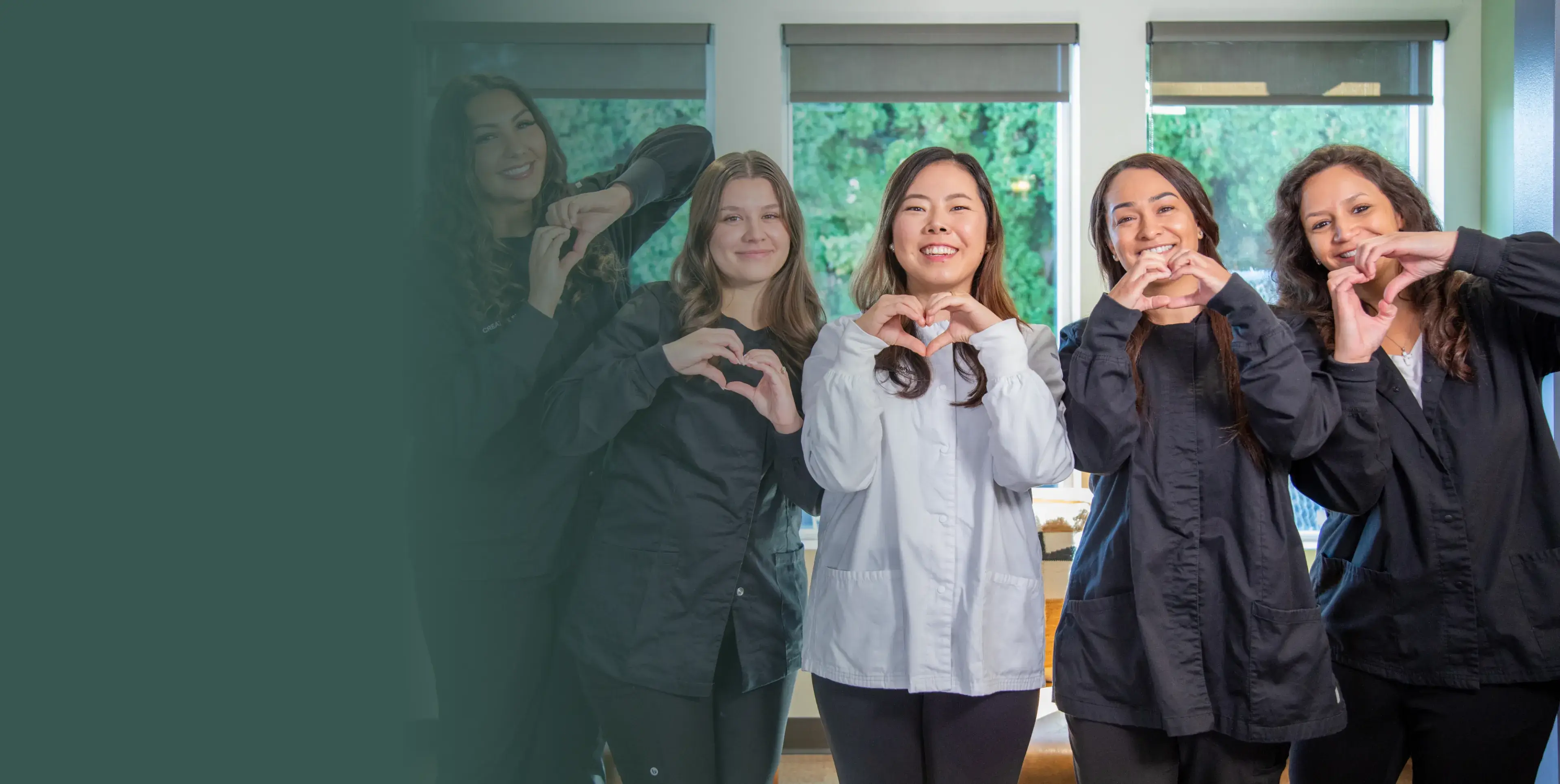 Four people stand indoors, smiling and making heart shapes with their hands.
