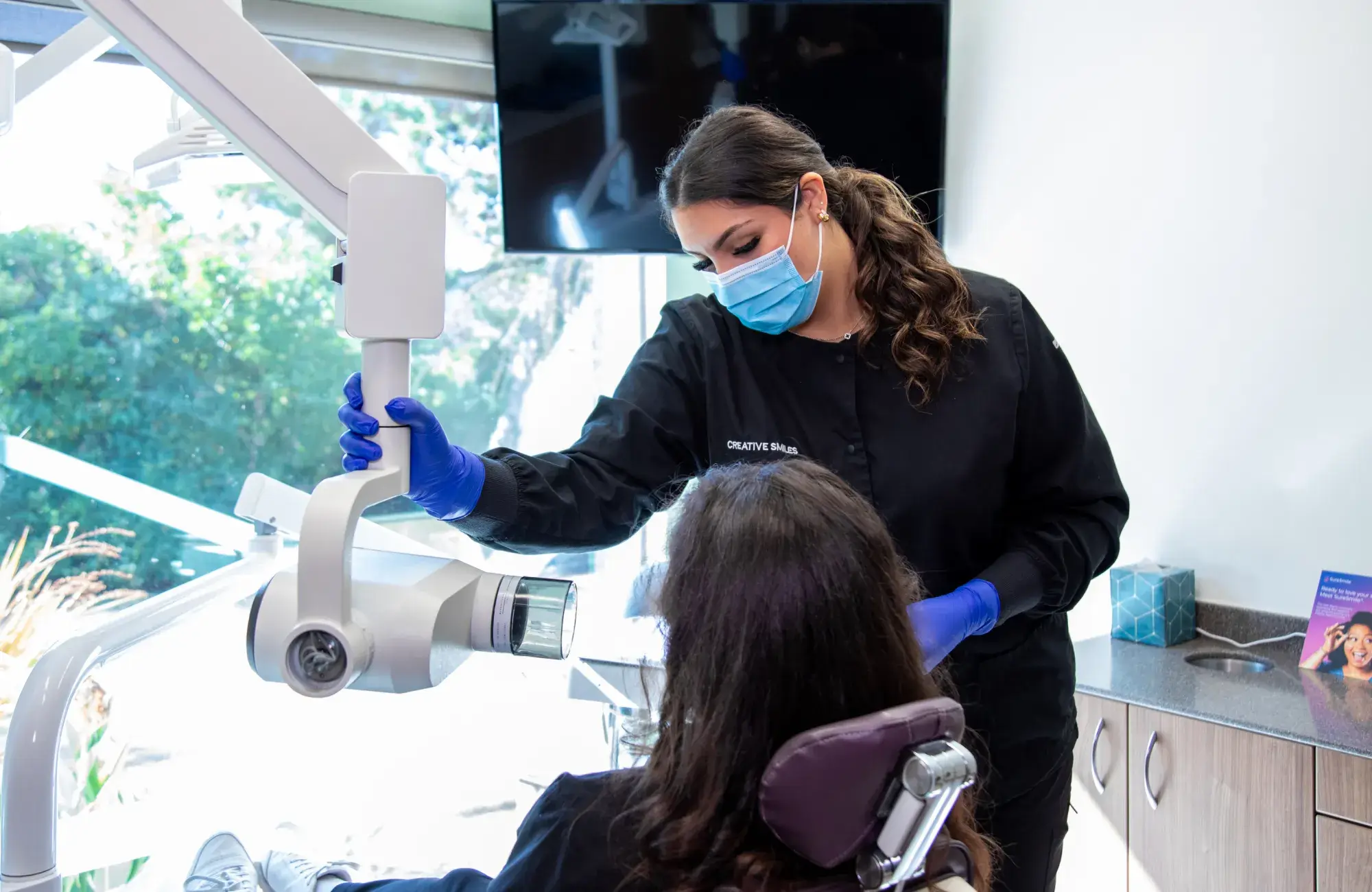 A dentist adjusts the light while examining a patient in a dental chair.