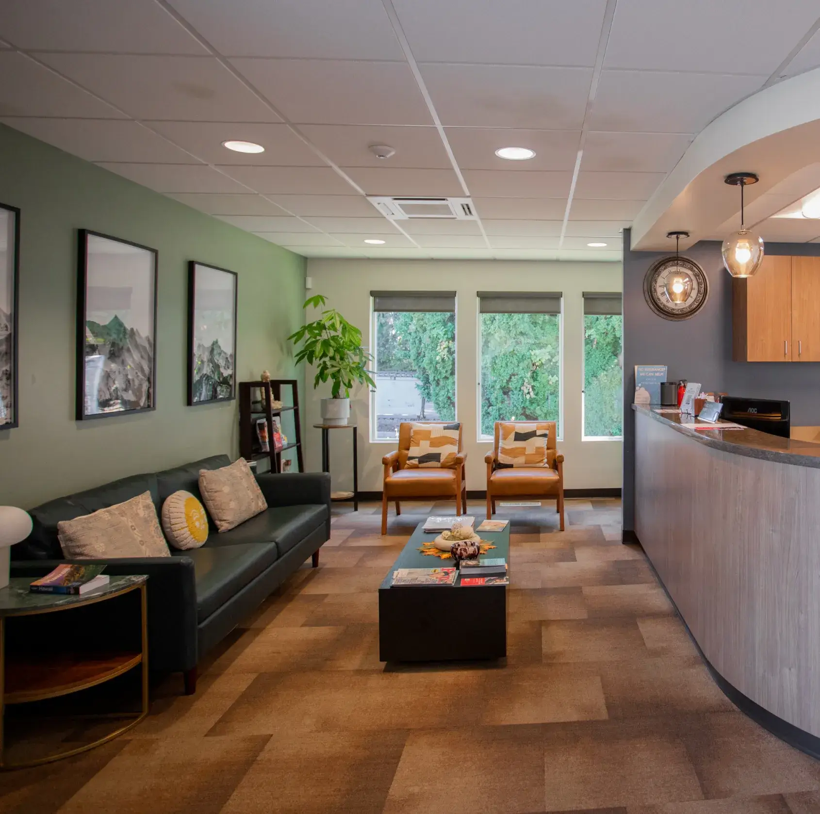 A waiting room with a black sofa, two chairs, and a curved reception desk.