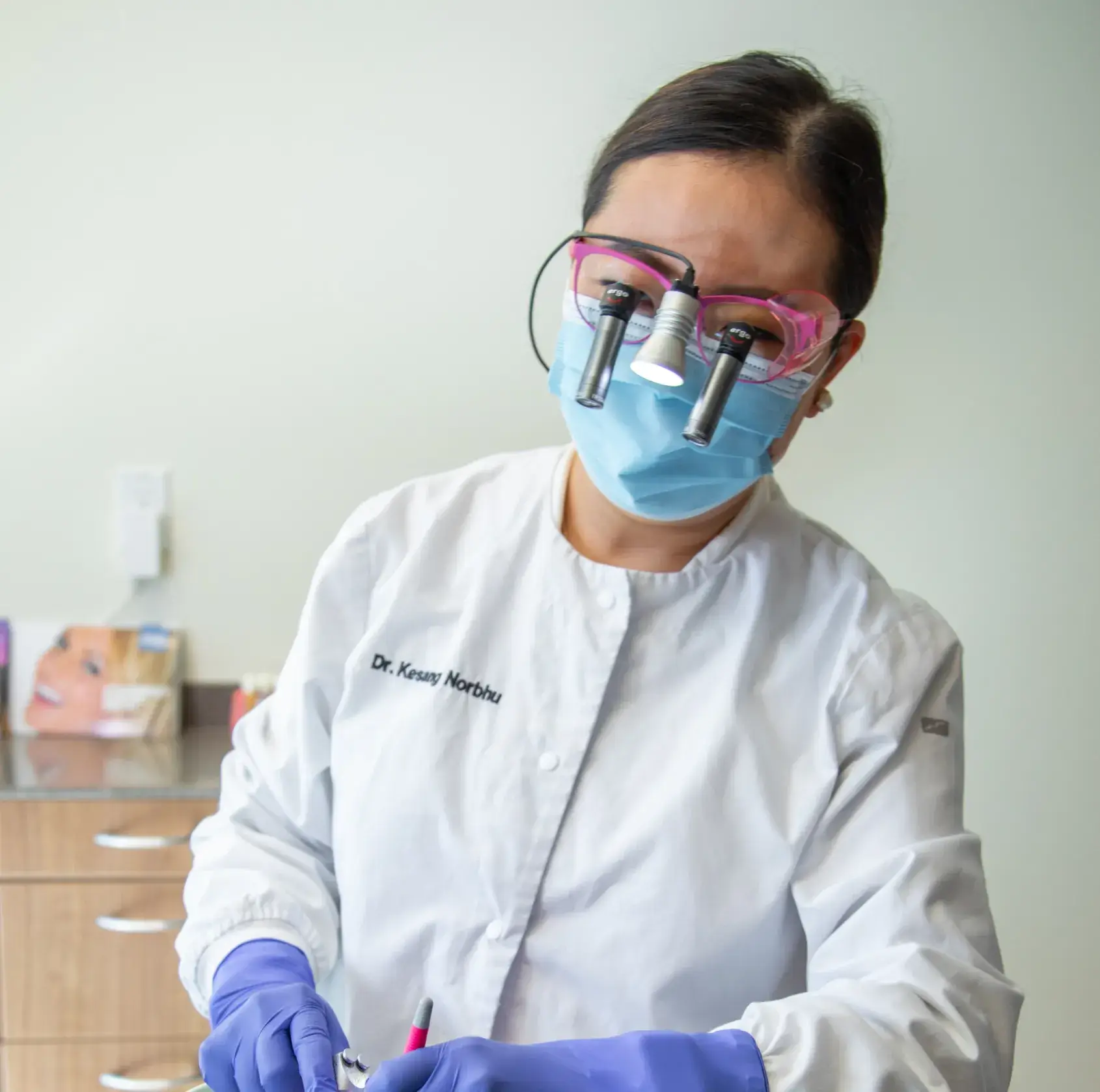 A dentist in a white coat wears magnifying glasses and gloves, performing a dental procedure.