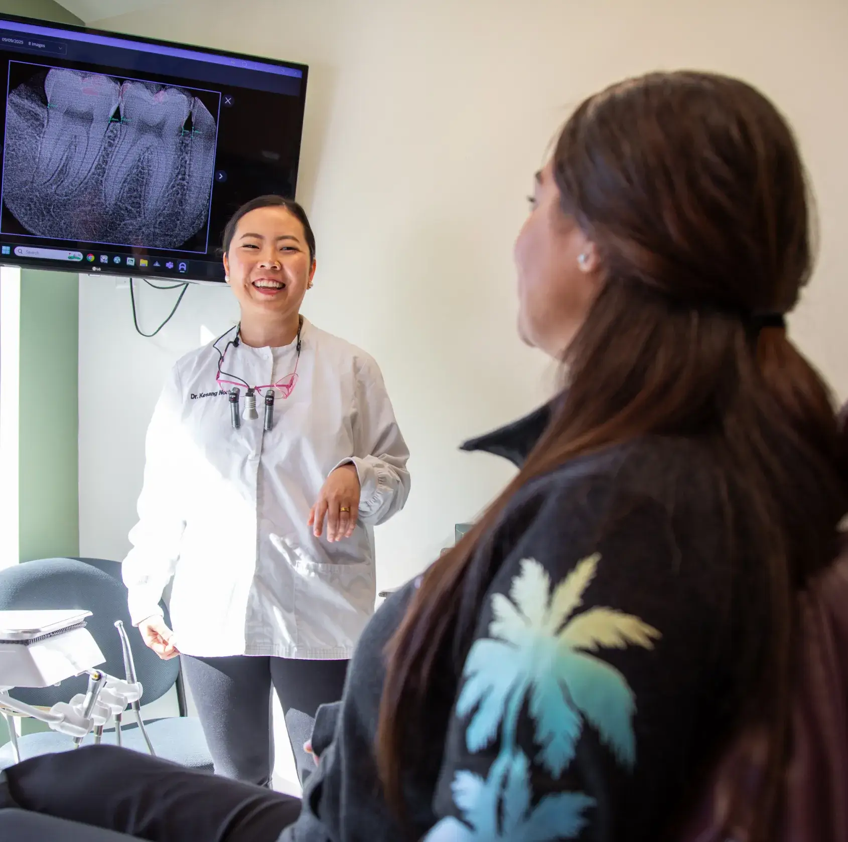 A dentist talks to a patient, showing dental X-rays on a screen in the exam room.