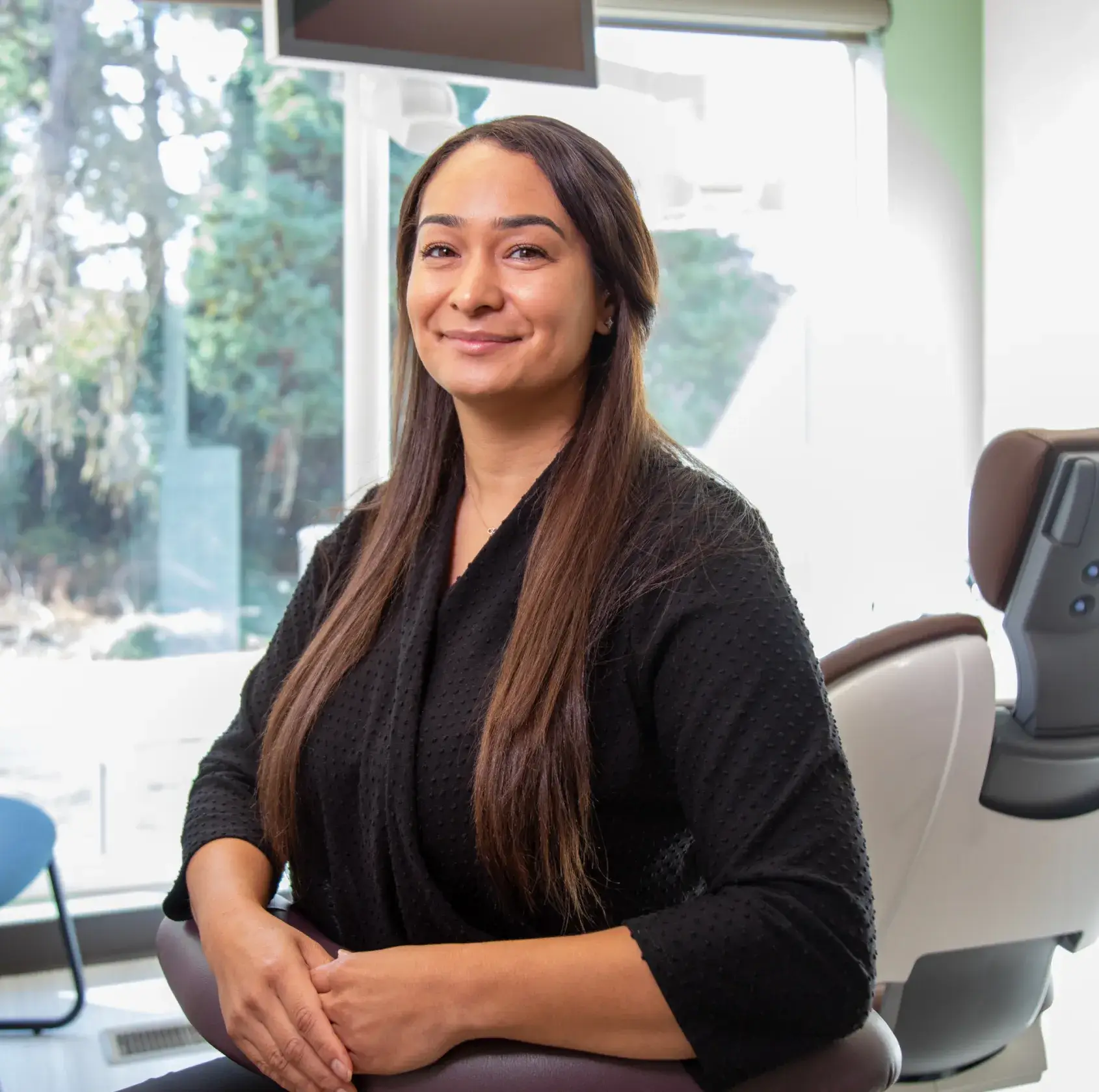 A woman with long hair smiles while sitting in a modern dental office.