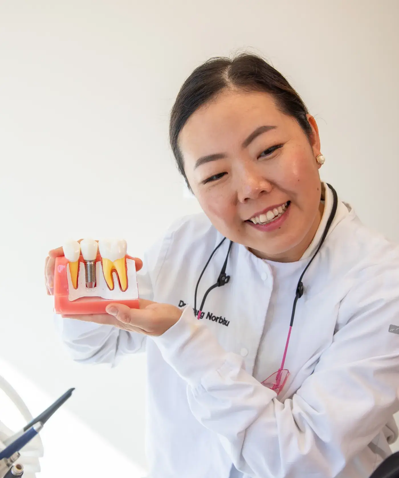 A dentist wearing a white coat holds a color-coded dental implant model, smiling at the camera.