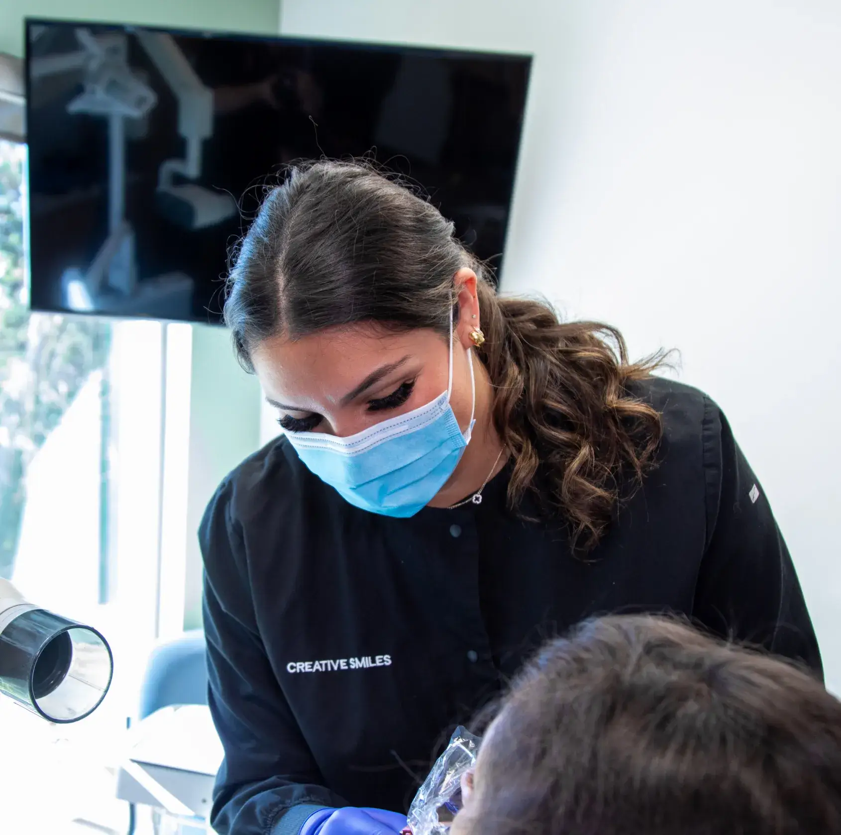 A dental professional wearing a mask examines a patient's teeth closely.