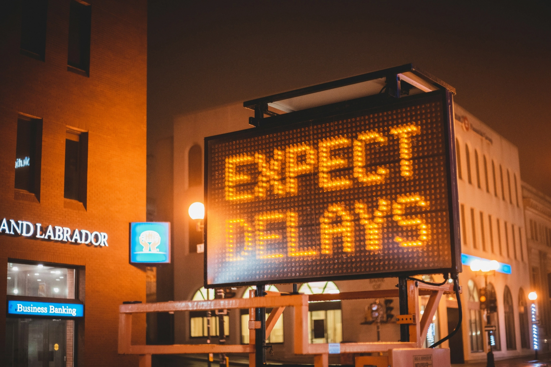Digital billboard displaying a brightly lit message 'Expect Delays' symbolizing ACH payment delays faced by merchants and retailers.