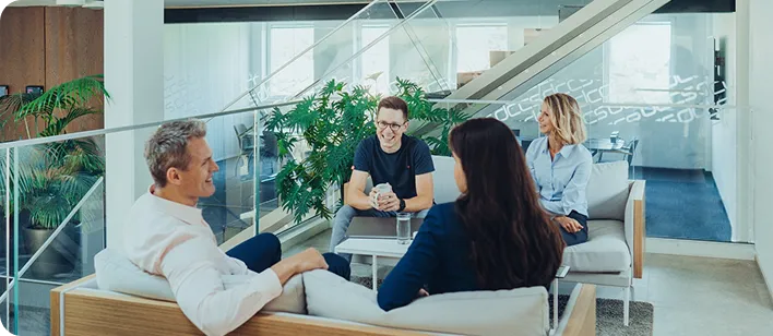 Vier Kollegen sitzen in einer modernen Büroumgebung und führen ein Gespräch.