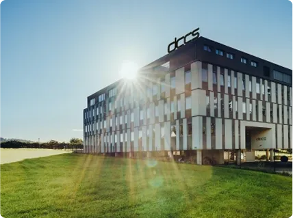 Modernes Bürogebäude mit der Aufschrift 'dkcs' bei Sonnenlicht und grüner Rasenfläche davor.