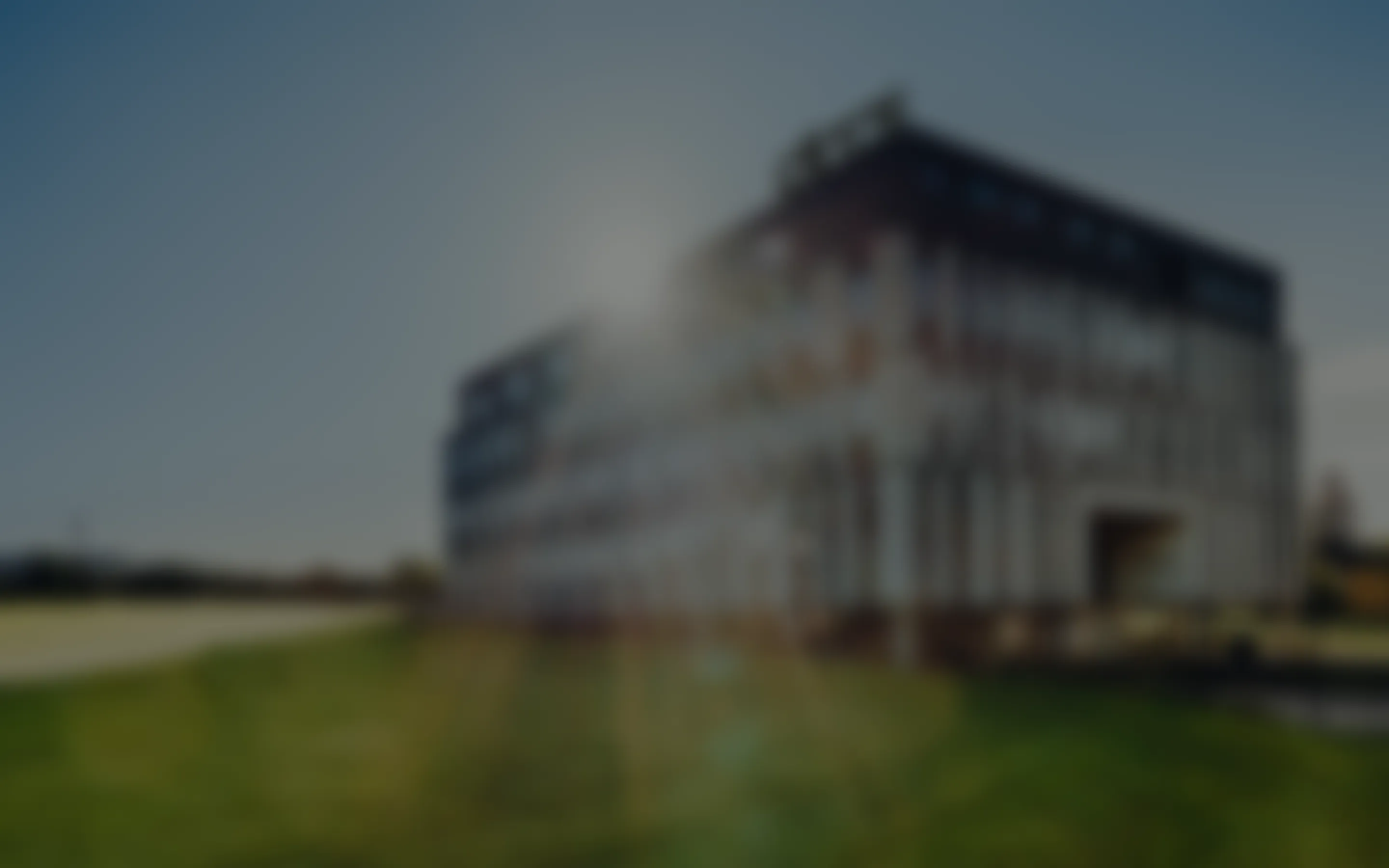 Unscharfes Bild eines modernen Bürogebäudes bei Sonnenlicht mit Rasen im Vordergrund.