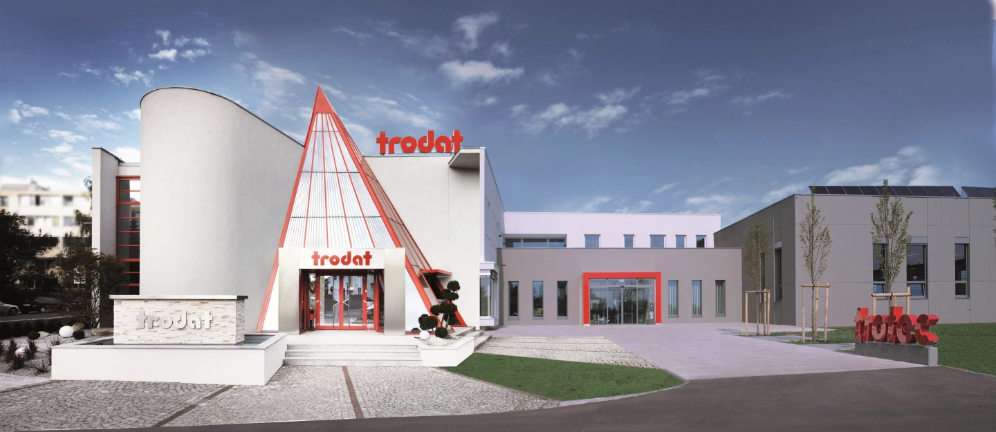 Moderne Firmengebäude von Trodat mit weißer Fassade, rotem Eingang und klarblauem Himmel.