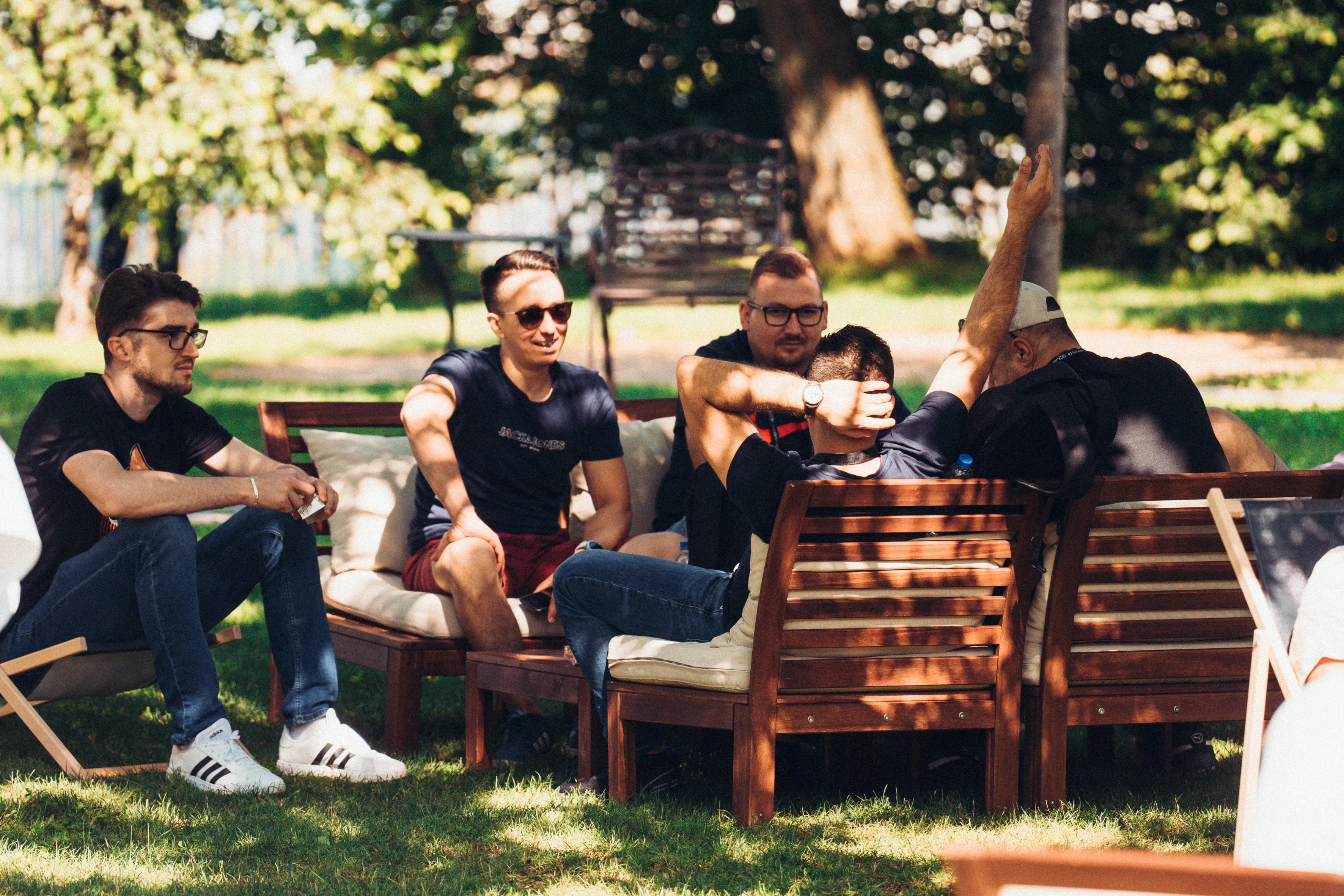 Fünf Männer sitzen bei sonnigem Wetter auf Gartenmöbeln im Freien und unterhalten sich entspannt.