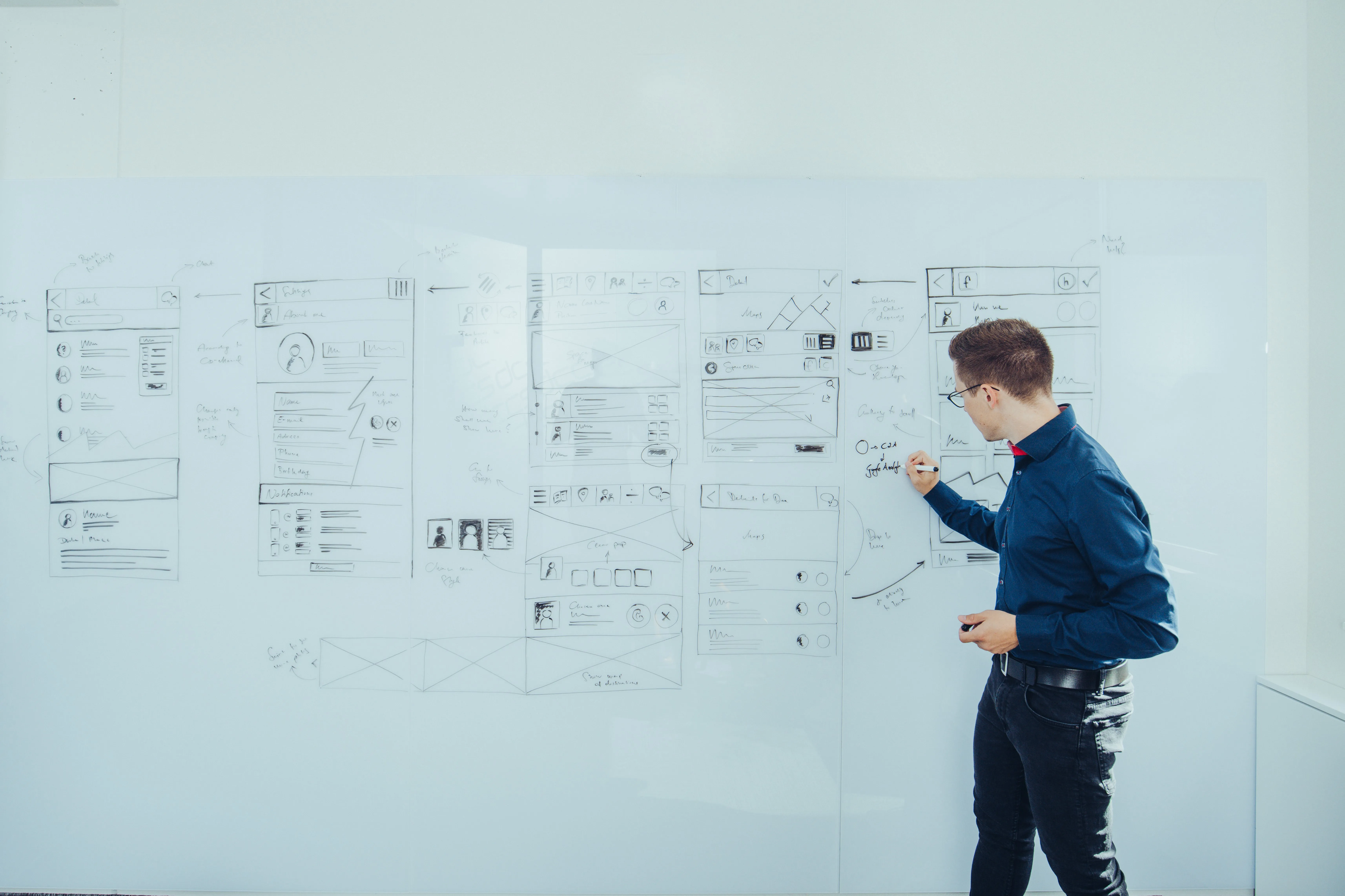 Mann schreibt vor einem weißen Whiteboard mit Skizzen und Entwürfen von App-Benutzeroberflächen.