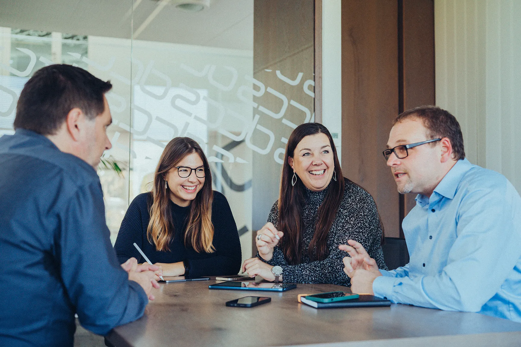 Vier Personen sitzen an einem Tisch und führen eine freundliche Besprechung in einem modernen Büro.