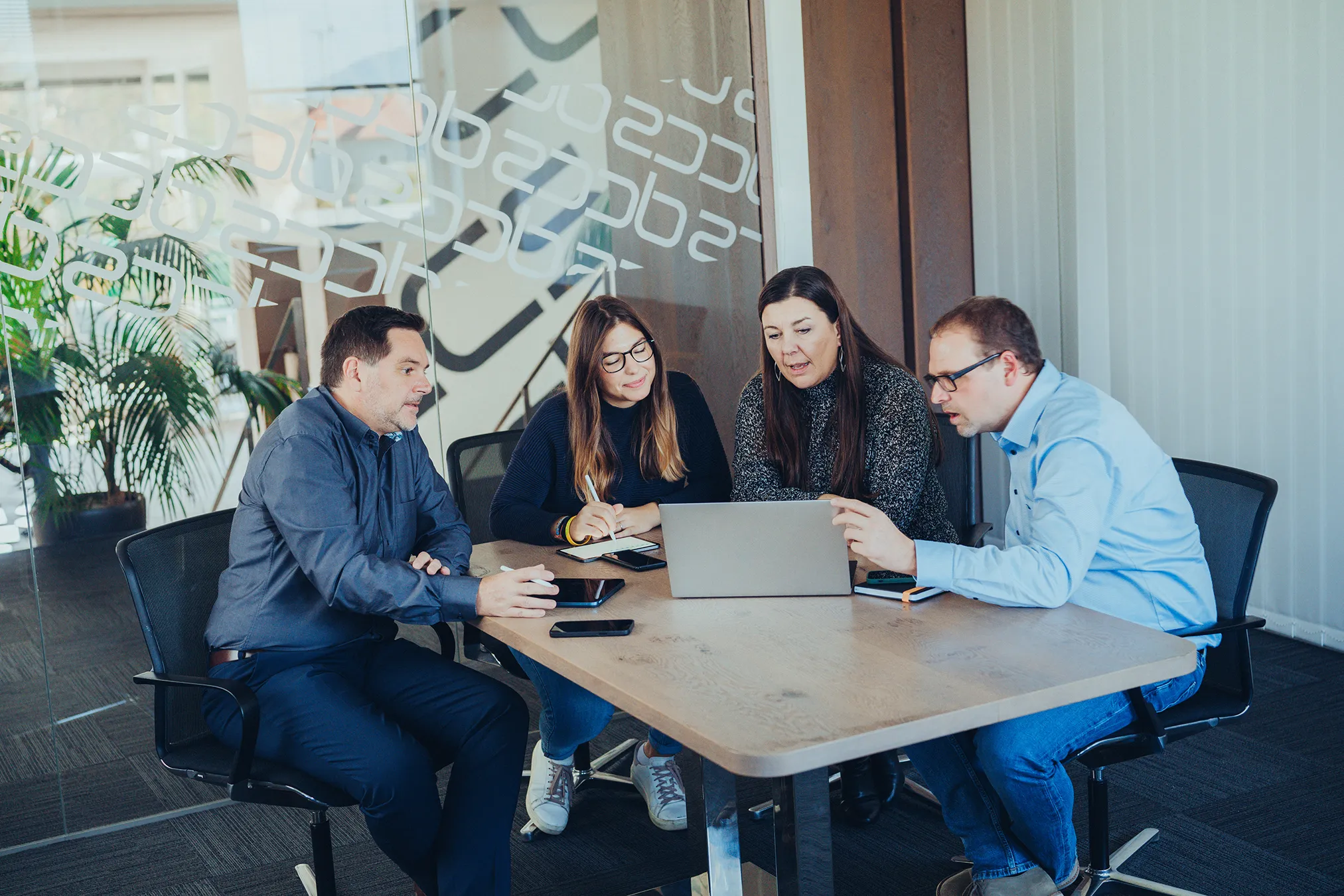 Vier Personen sitzen um einen Tisch und arbeiten gemeinsam an einem Laptop in einem modernen Büro.