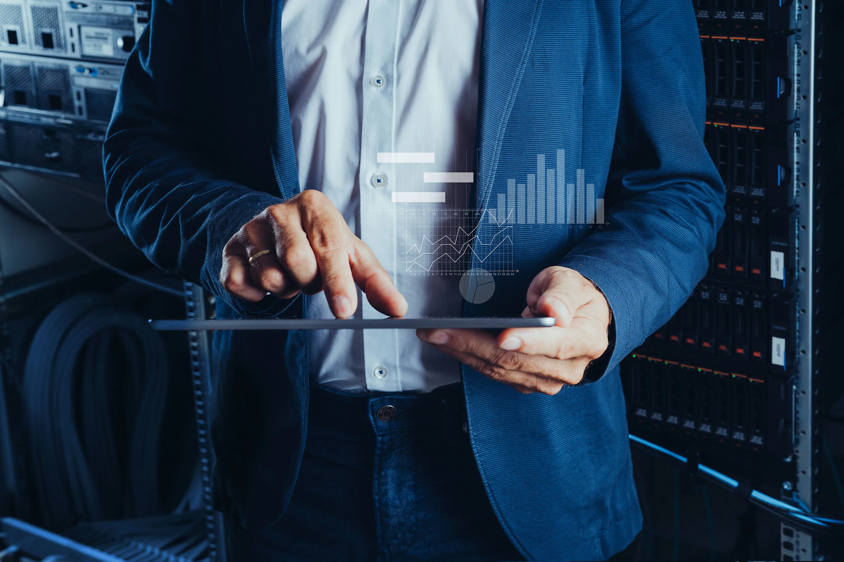 Geschäftsmann im Anzug bedient Tablet mit überlagerten Diagrammen in einem Serverraum.