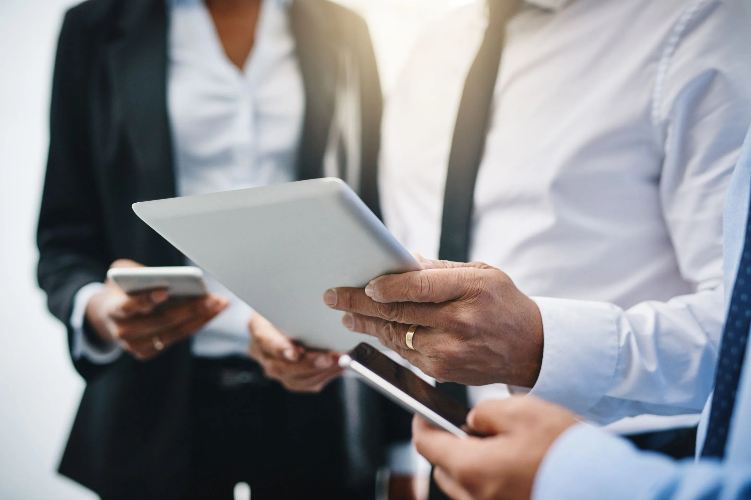 Geschäftspersonen in formeller Kleidung, die Tablets und Smartphones in der Hand halten.