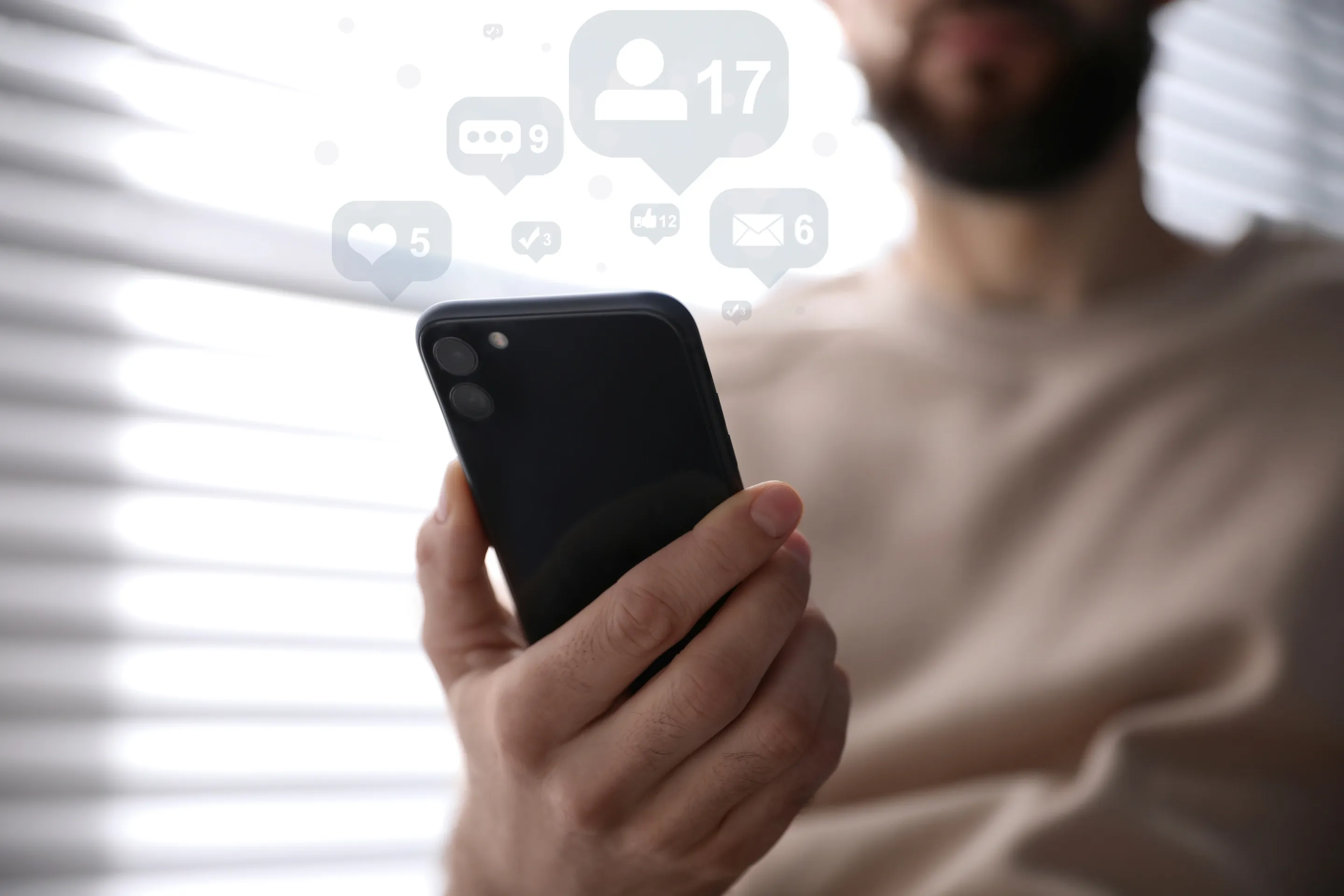 Mann hält Smartphone, umgeben von Symbolen sozialer Medien mit Benachrichtigungen für Nachrichten, Freundschaftsanfragen und Likes.