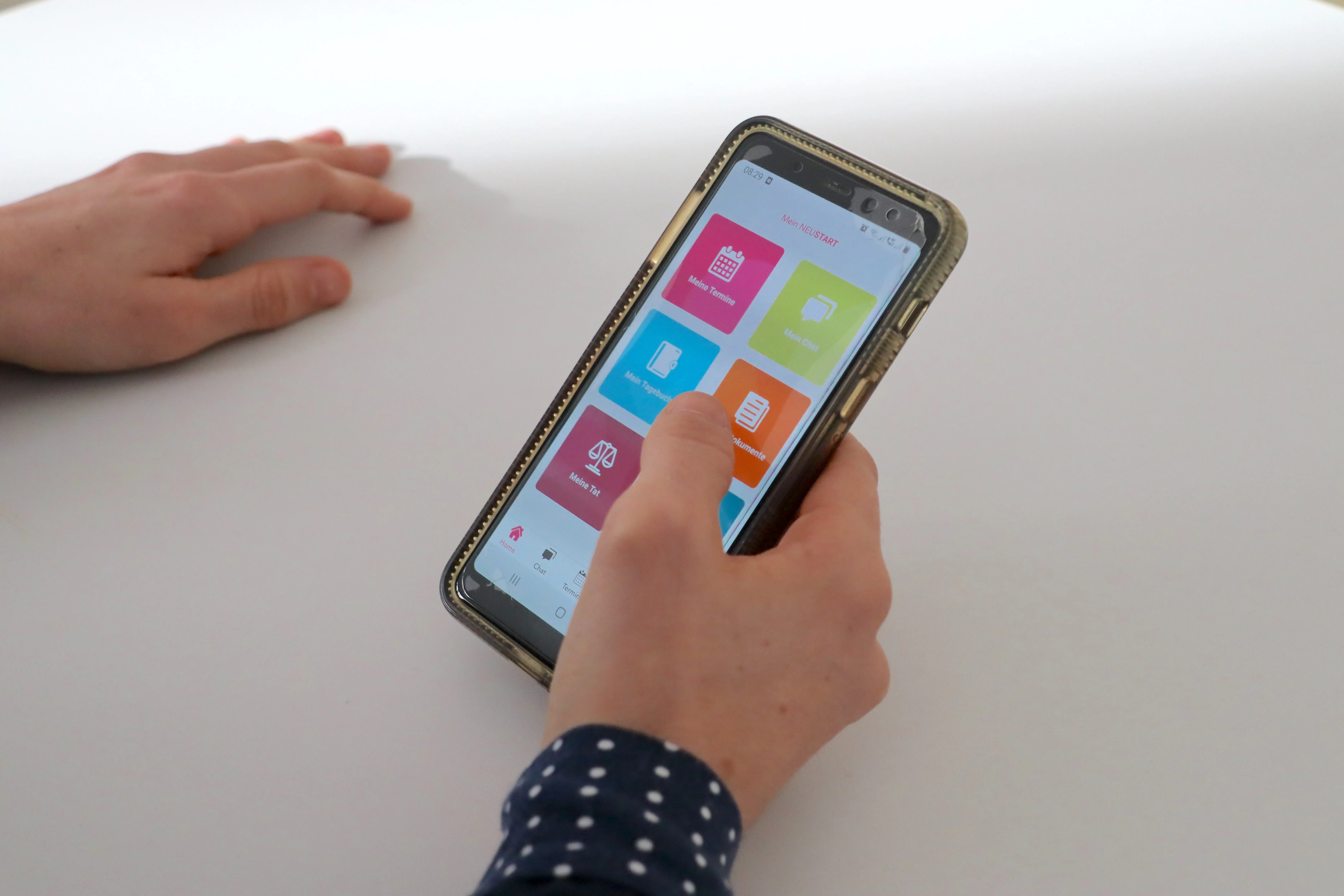 Hand hält Smartphone mit einer App-Oberfläche, die farbige Kacheln mit deutschen Texten wie 'Meine Termine' und 'Meine Dokumente' zeigt.