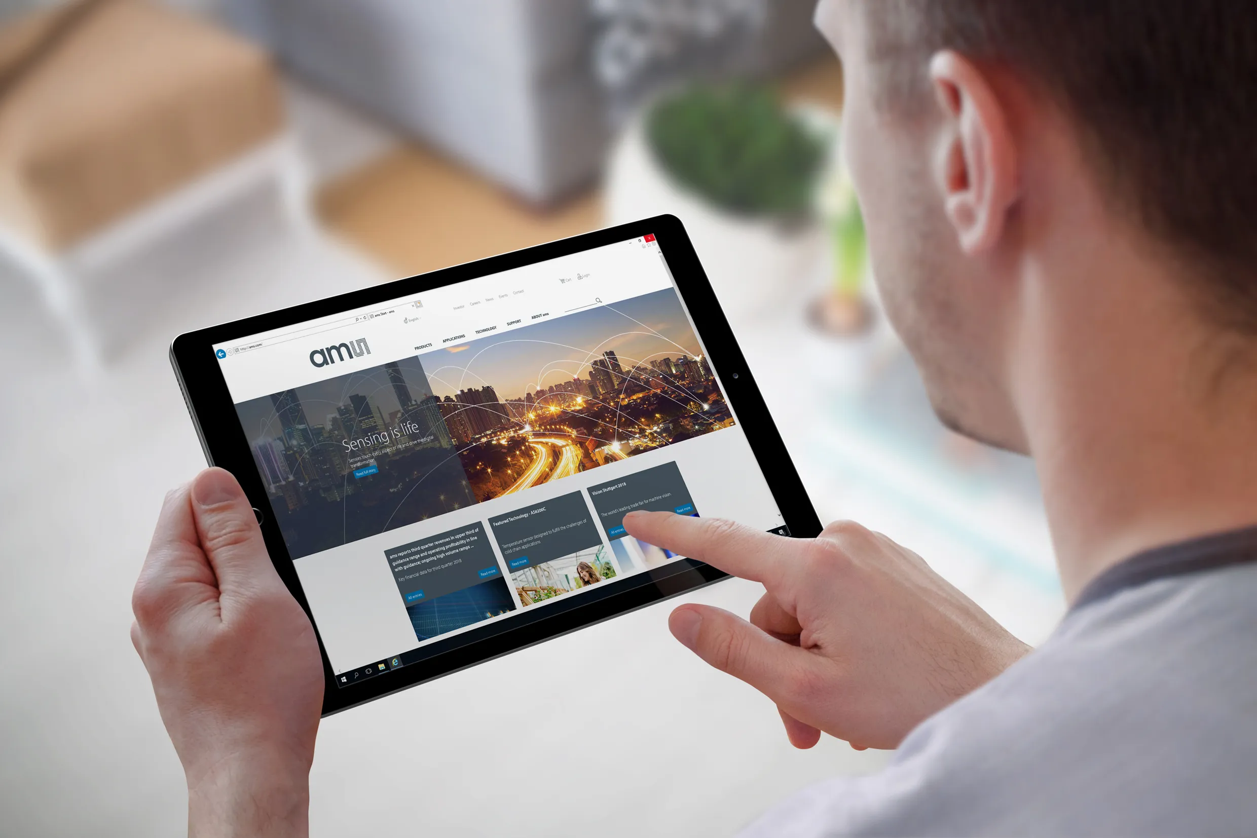 Person hält ein Tablet und sieht sich die ams-Website mit dem Slogan 'Sensing is life' an.