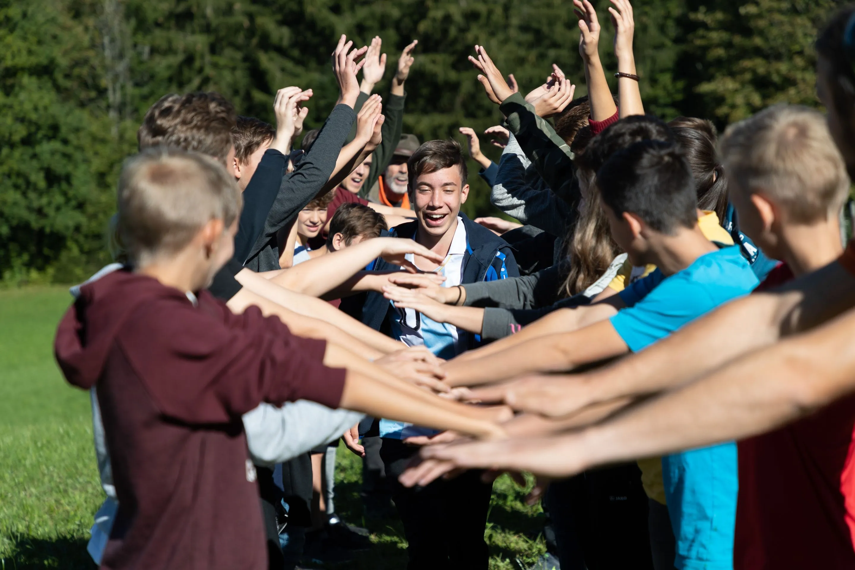 Gruppe Jugendlicher bildet eine Menschenstraße mit erhobenen Armen, während ein lachender Junge in der Mitte hindurchgeht.