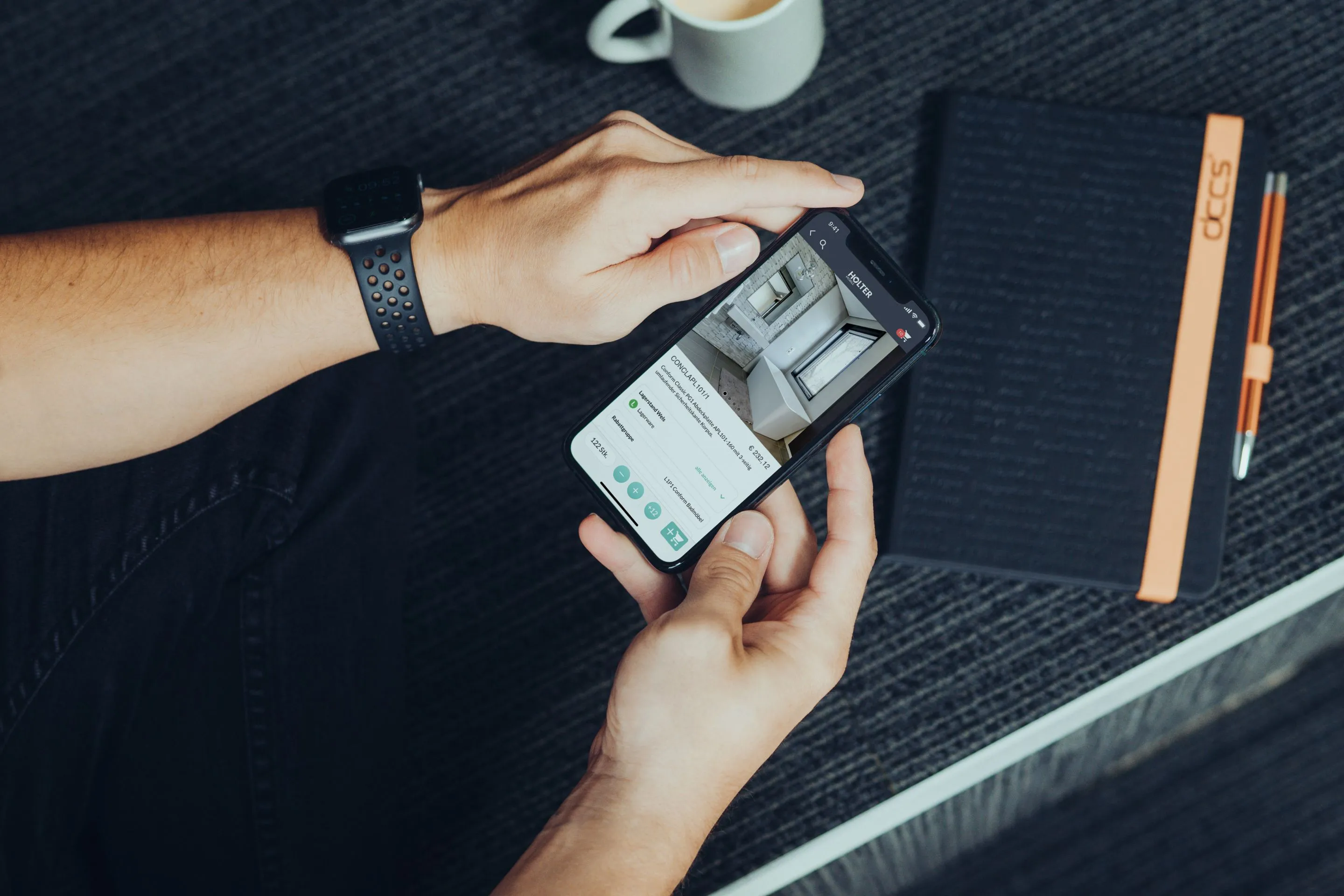 Person hält ein Smartphone mit einer Immobilien-Website neben einem Notizbuch, Stift und einer Tasse Kaffee.