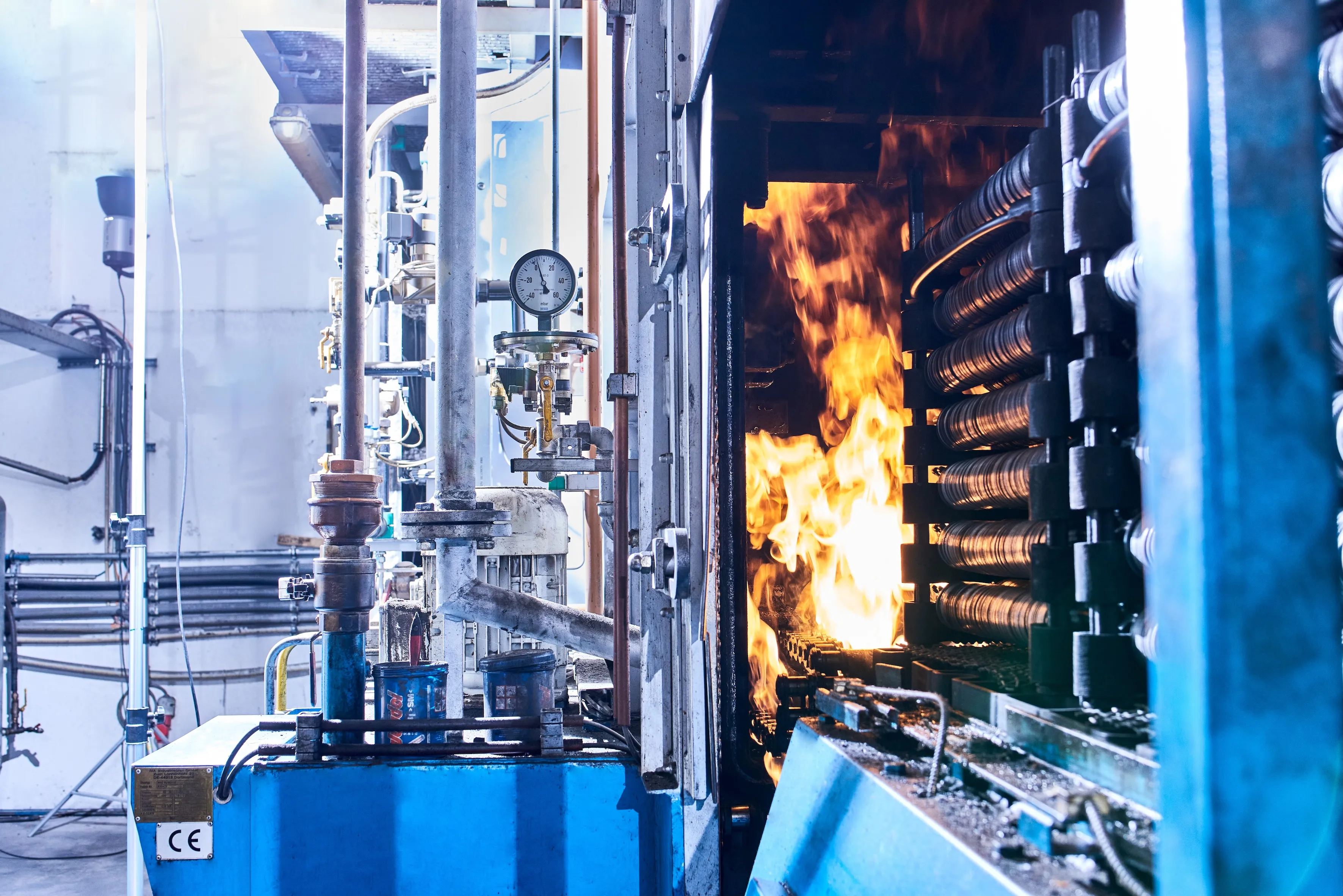 Industrieofen mit sichtbarer Flamme und Metallrollen in einer Fabrikumgebung.