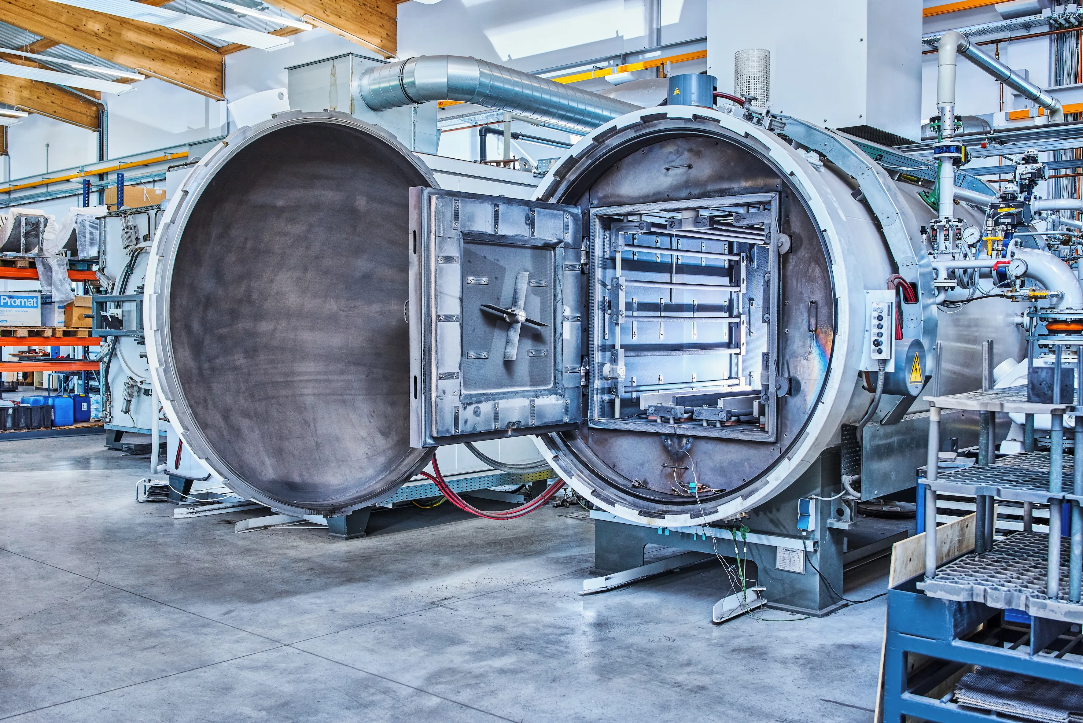 Große industrielle Autoklavmaschine mit geöffneten runden Türen in einer Fertigungshalle.