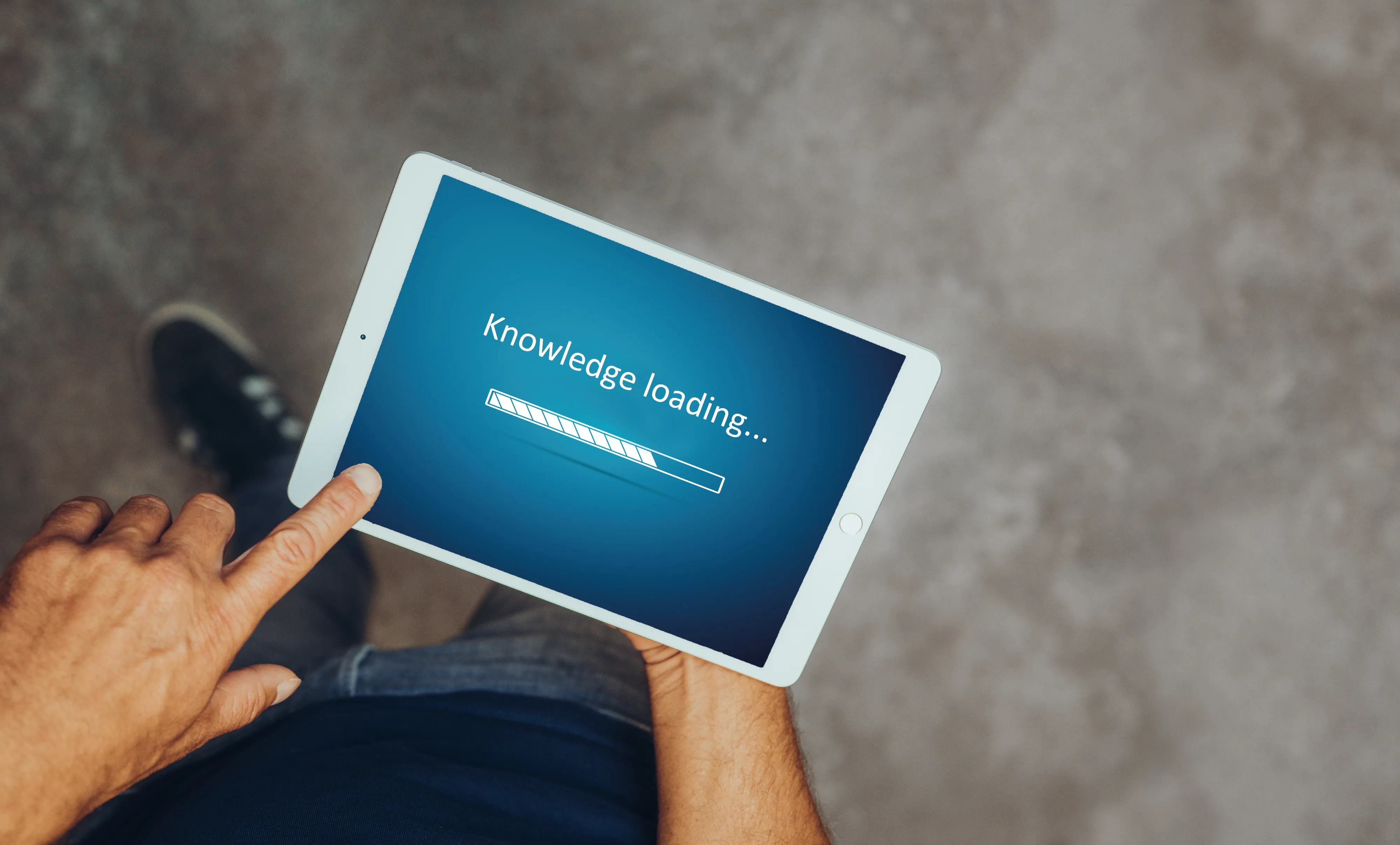 Person hält ein Tablet mit einem Ladebalken und dem Text 'Knowledge loading...'.