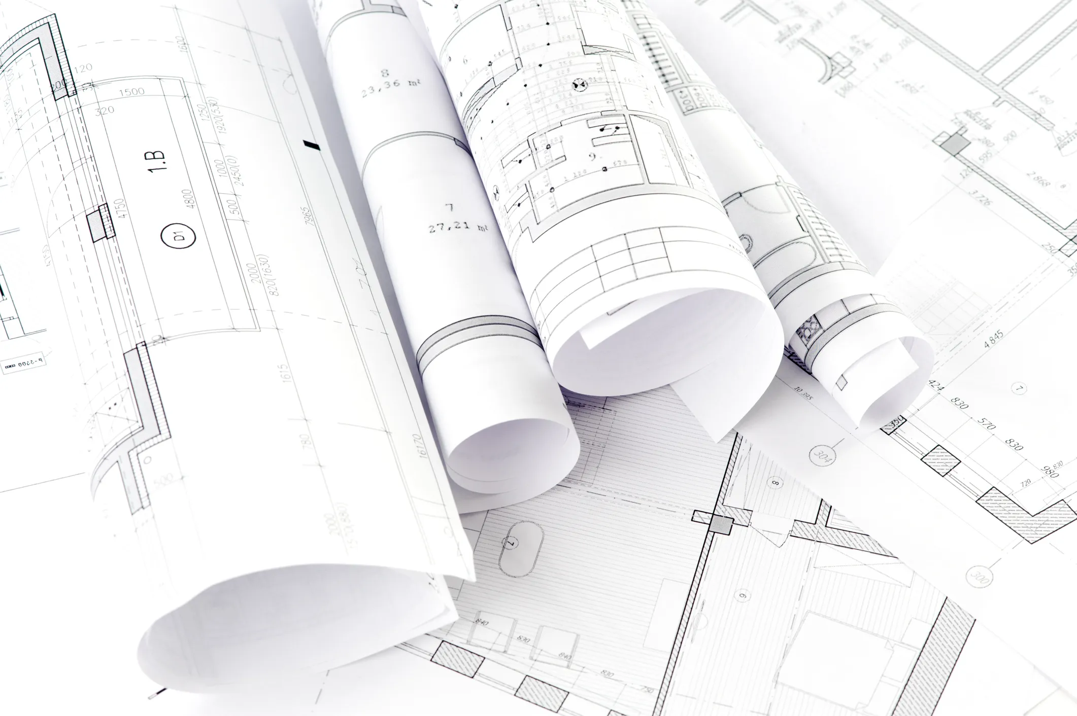 Rollen von Architekturplänen liegen auf ausgelegten technischen Bauzeichnungen.
