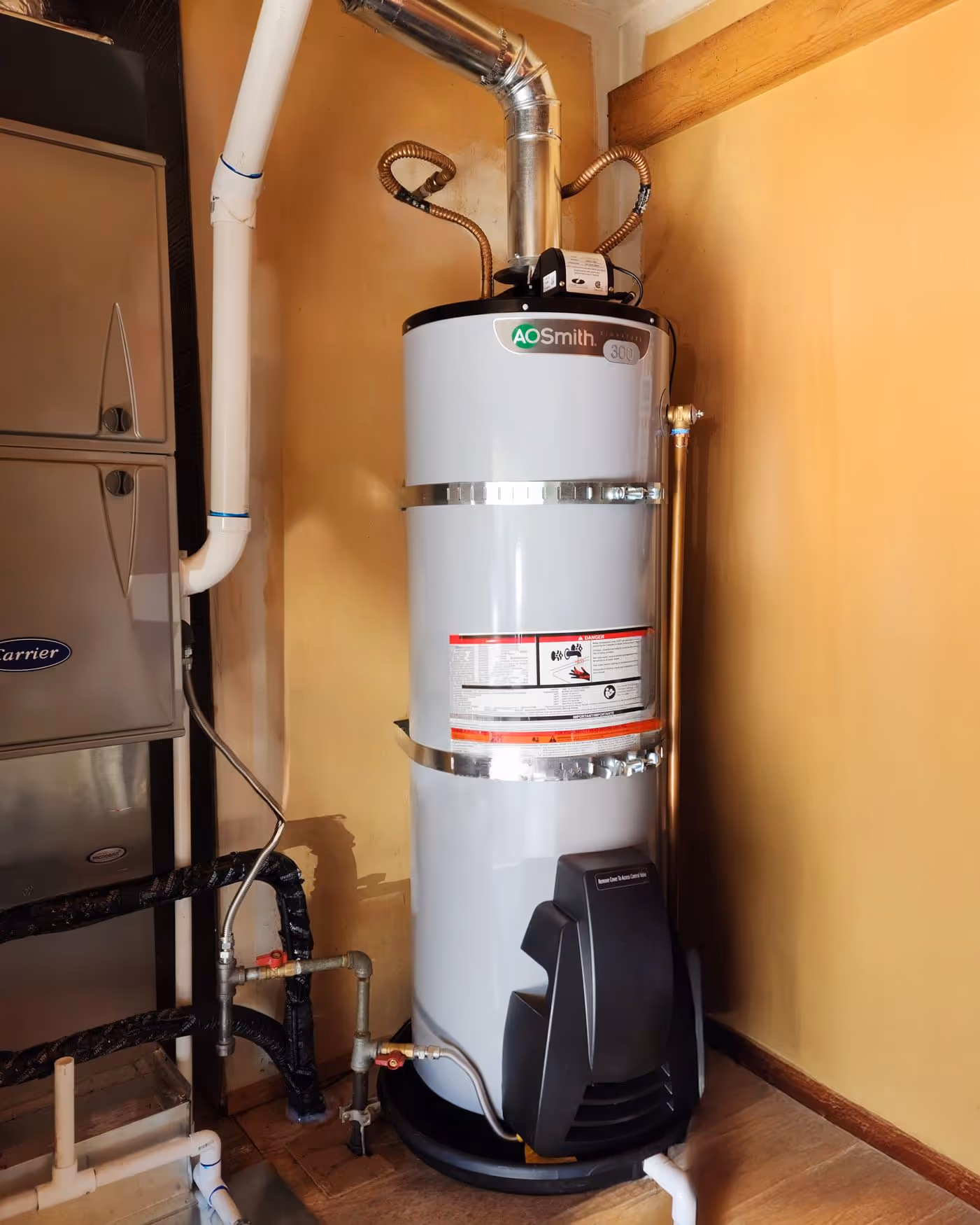 AO Smith branded electric water heater installed in a corner next to HVAC unit with connected pipes.