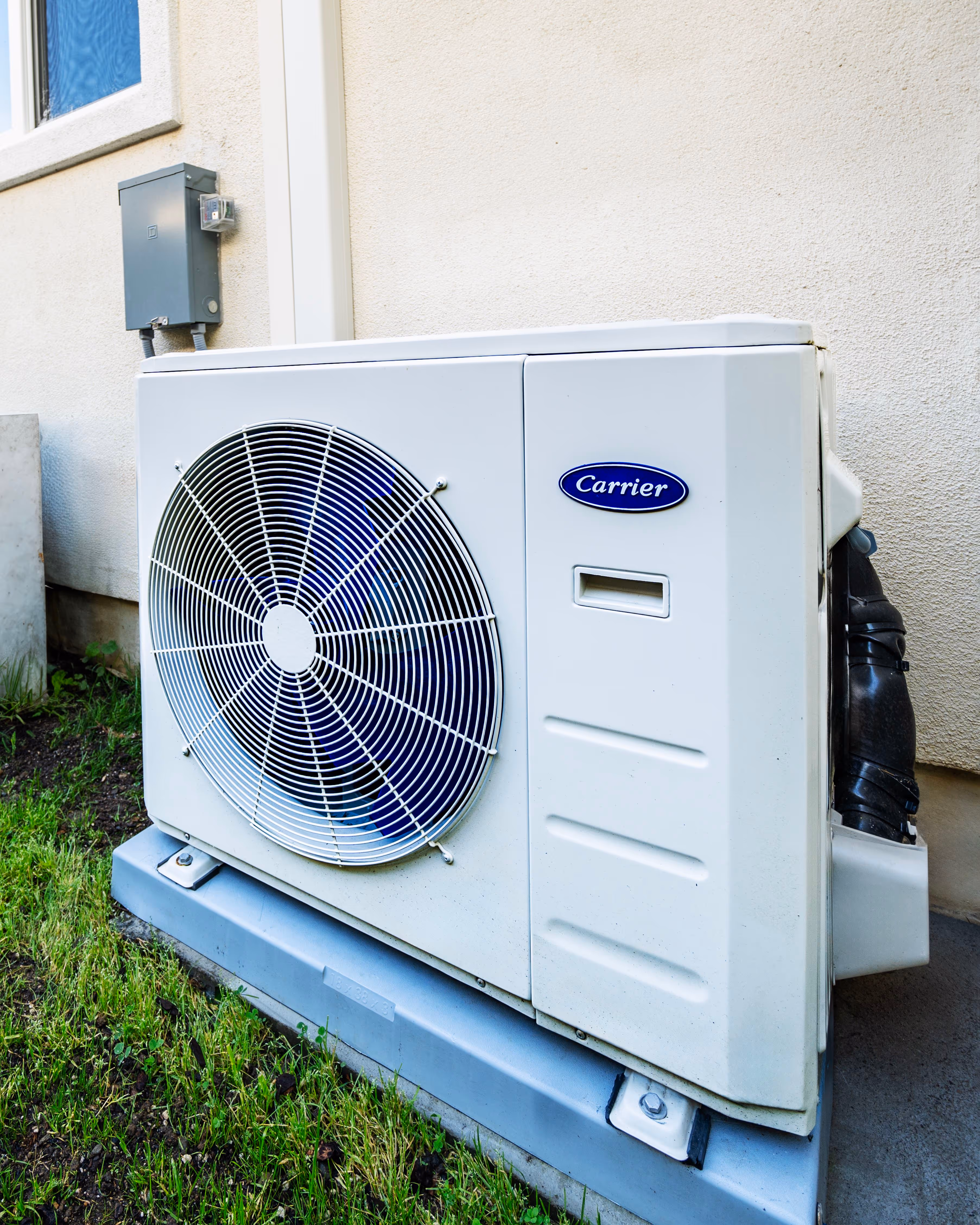 Outdoor Carrier air conditioning unit installed on the ground beside a building wall.