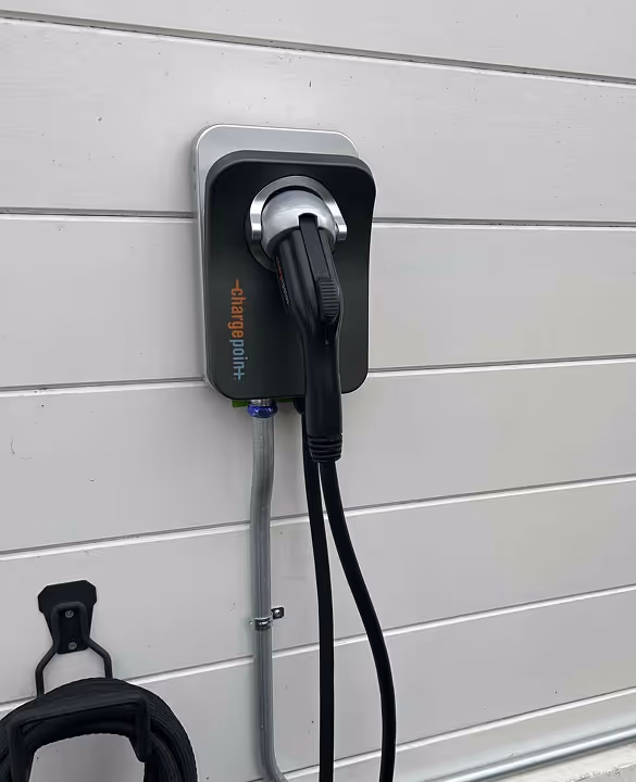 Electric vehicle charging station mounted on a white wall with a black charging cable plugged in.