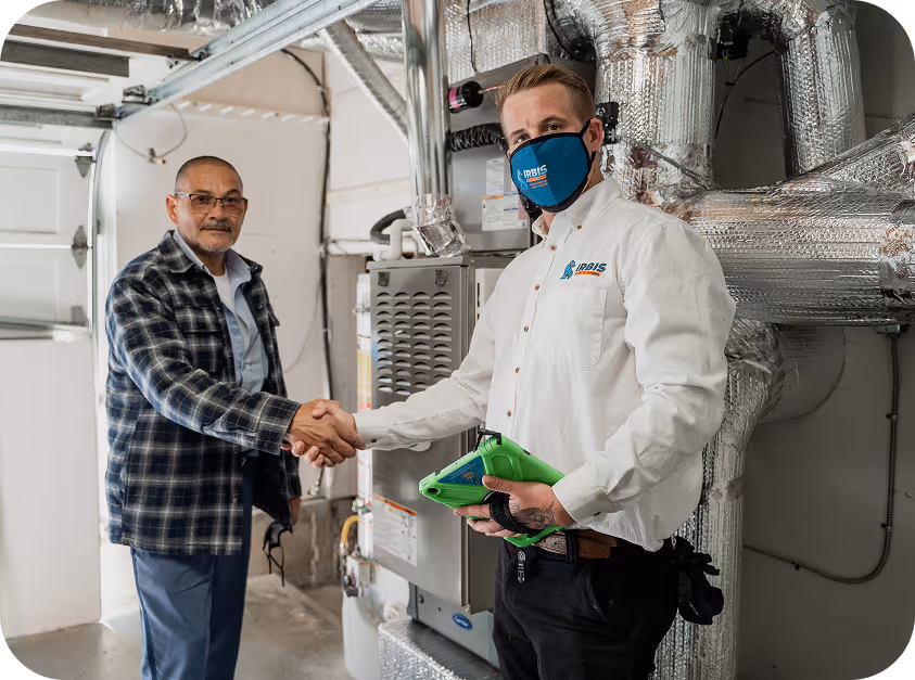 Technician and homeowner shaking hands near HVAC system in a garage.