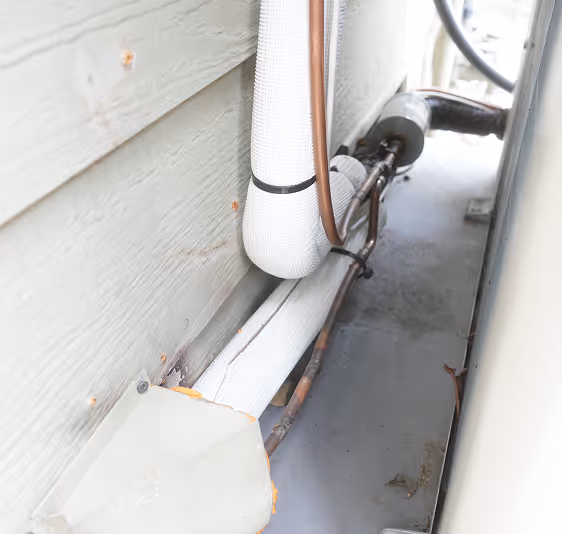 Insulated pipes running along the narrow exterior space between two walls.