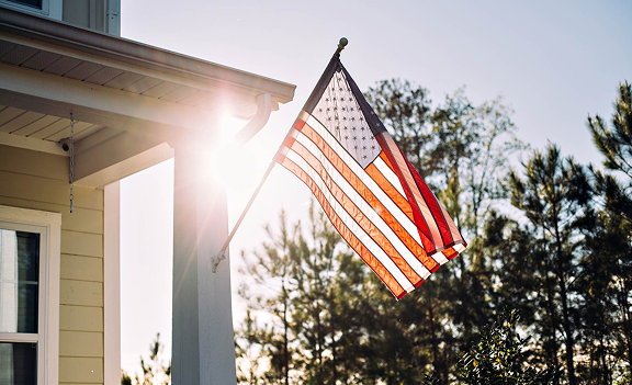 An American flag with the sun shining through it on the front porch of a house