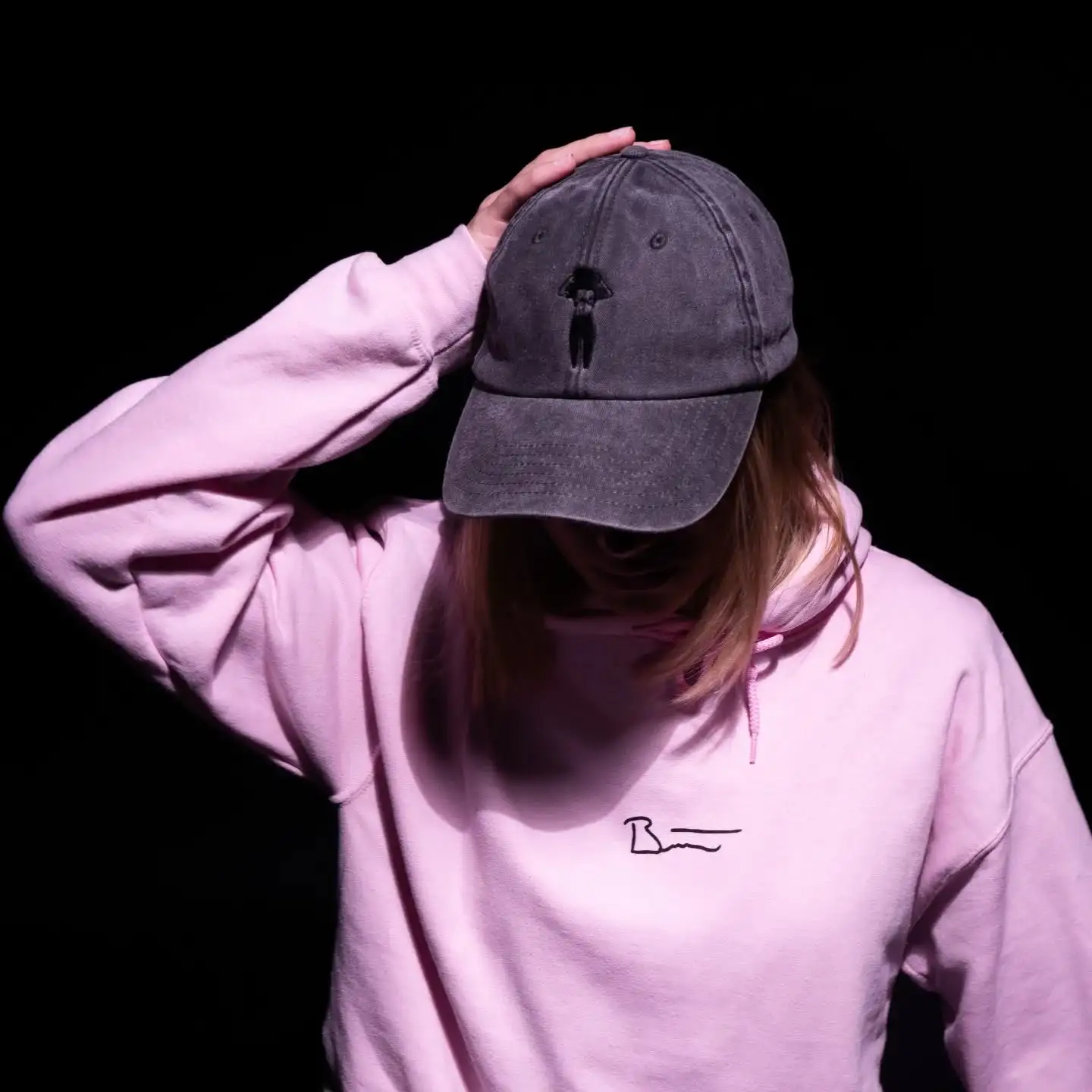 Person mit grauer Kappe mit dezenter Stickerei und rosa Pullover.