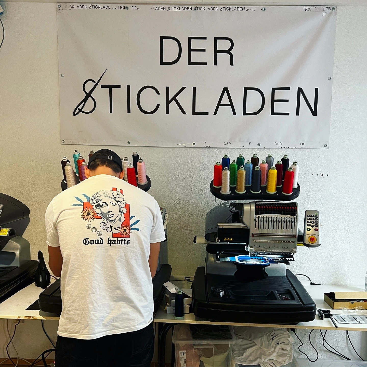 Pascal in weißem T-Shirt mit großer Rückenstickerei beim Arbeiten an Stickmaschinen.