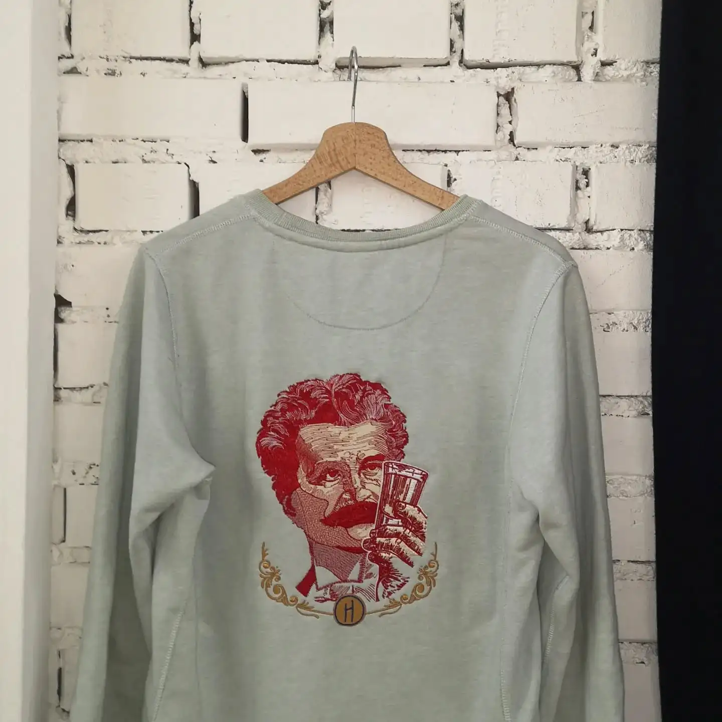 Langarmshirt mit detailreicher roten Stickerei eines Gesichts auf einem Kleiderbügel.