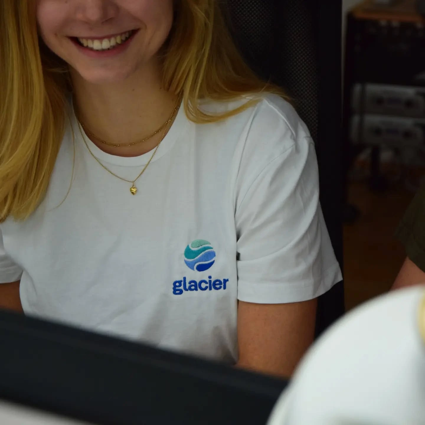 Frau trägt ein weißes T-Shirt mit blauer „glacier“-Stickerei und lächelt.